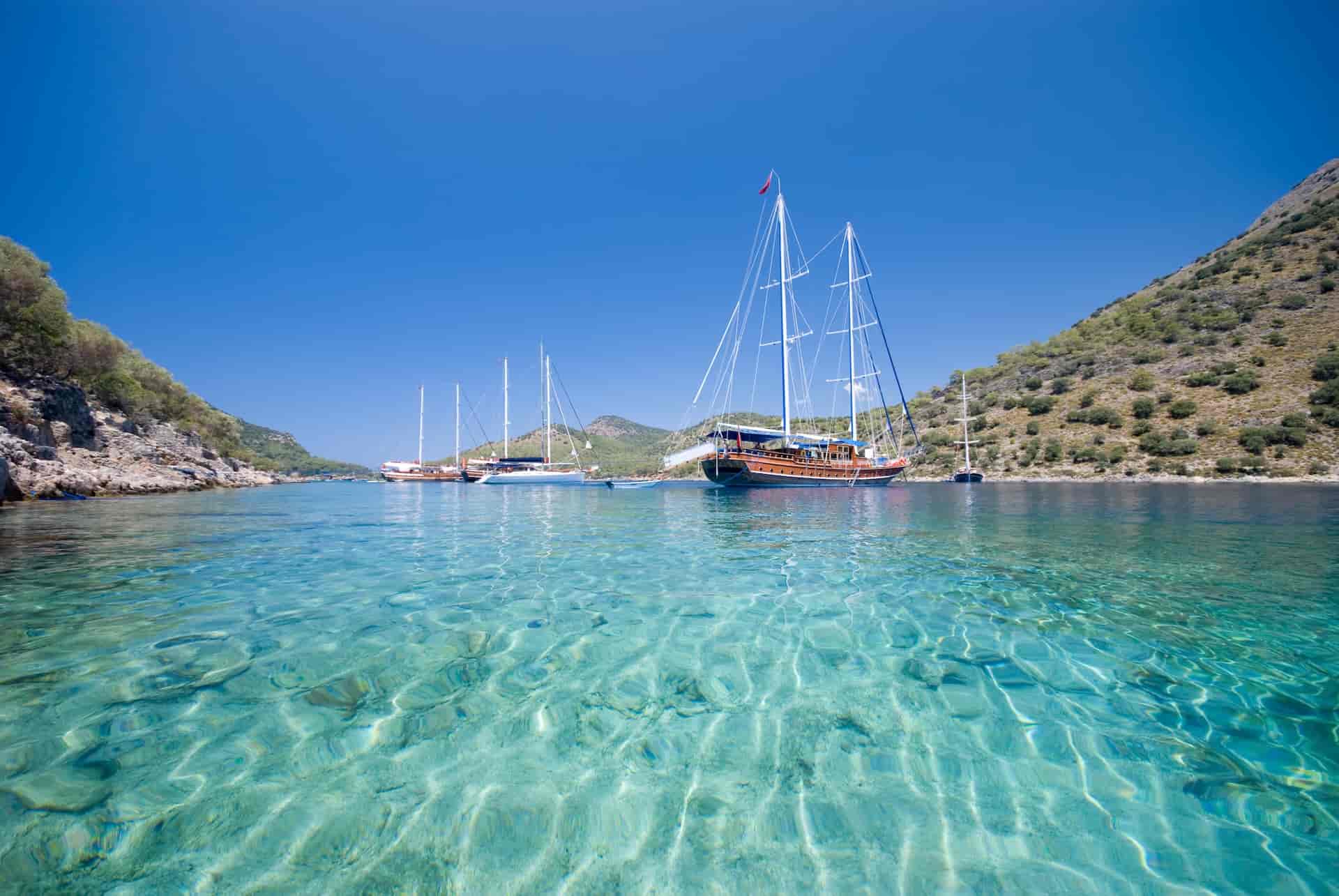 Gulets anchored in secluded bay with turquoise water and arid hillsides