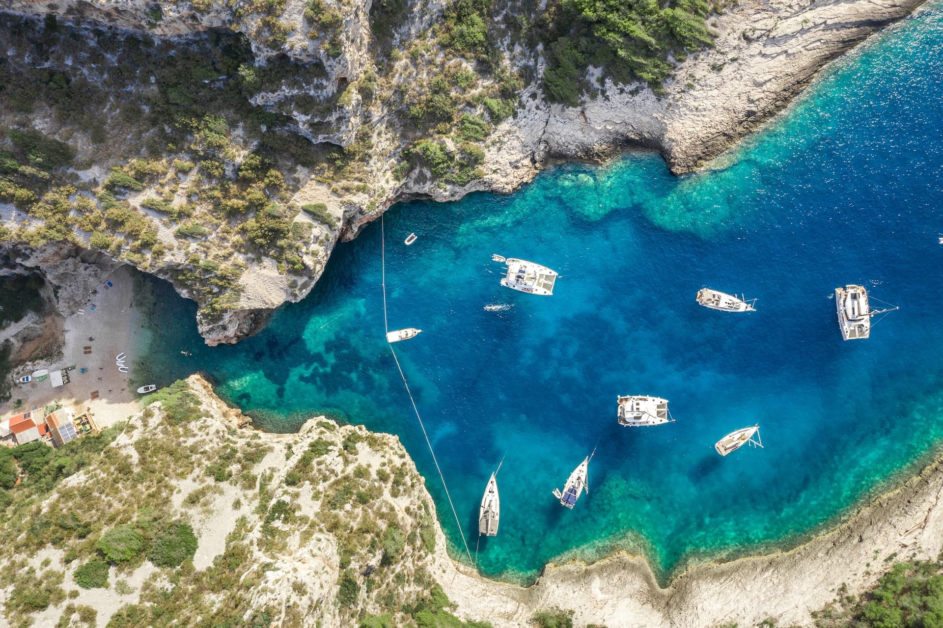 Boats anchored in turquoise cove waters surrounded by steep, scrub-covered cliffs in Komiza Bay.