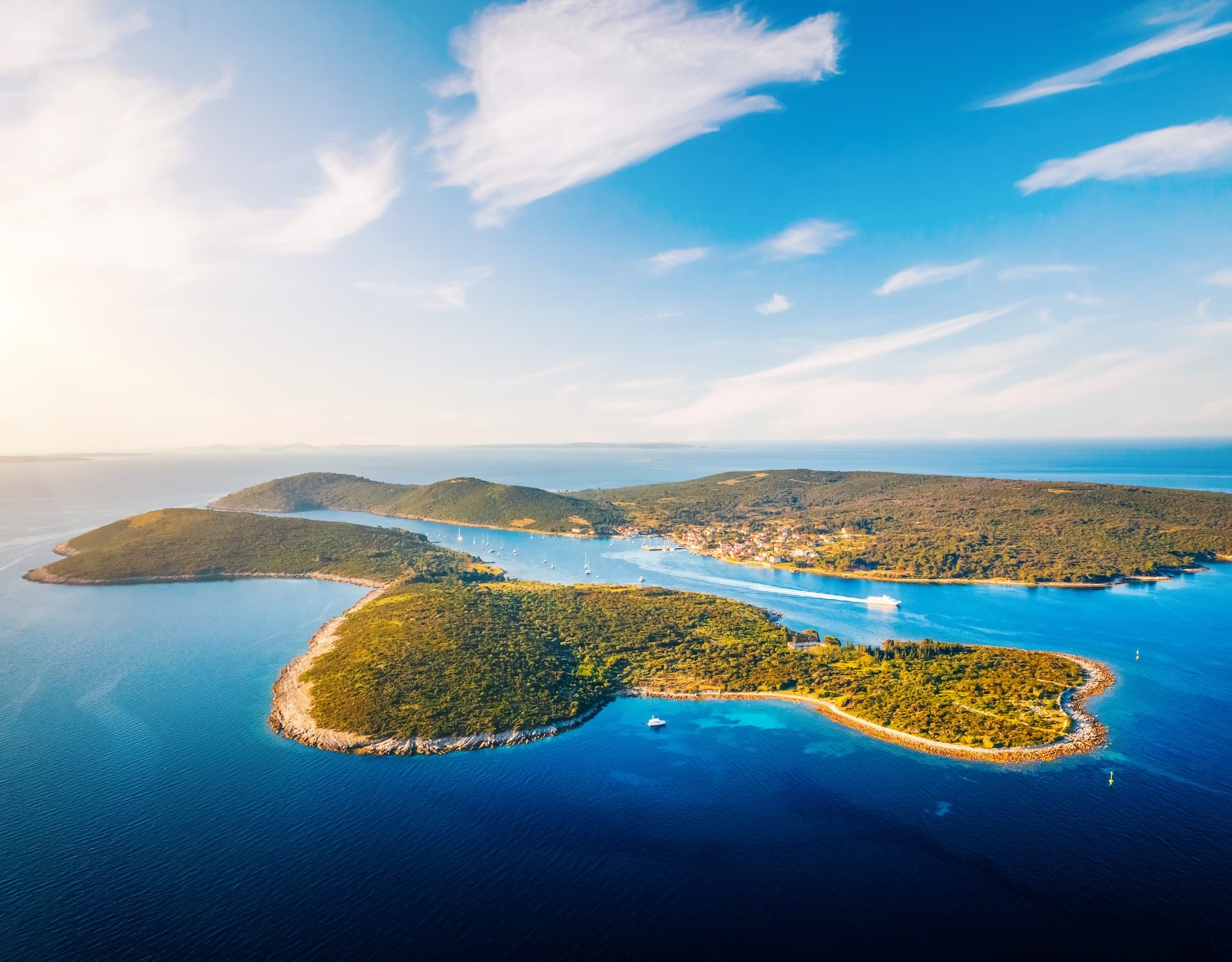 Aerial view of Croatian islands with lush green hills, blue sea, and small coastal town.