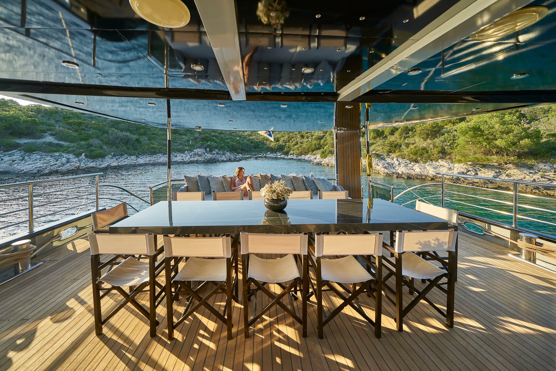 Yacht deck dining area with teak floor overlooking a rocky, tree-lined cove