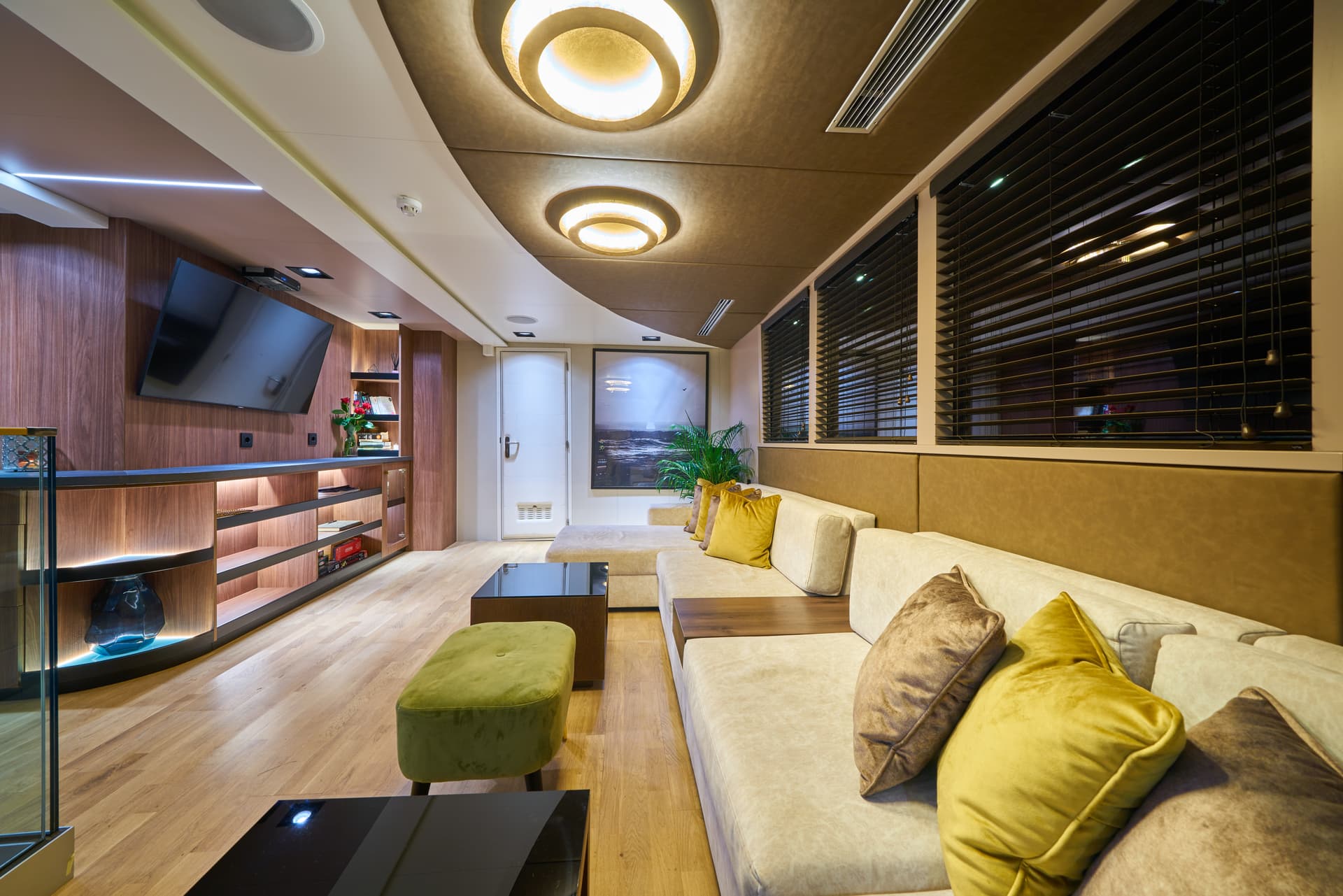 Luxurious yacht saloon interior with wood paneling, large sofa, and modern lighting.