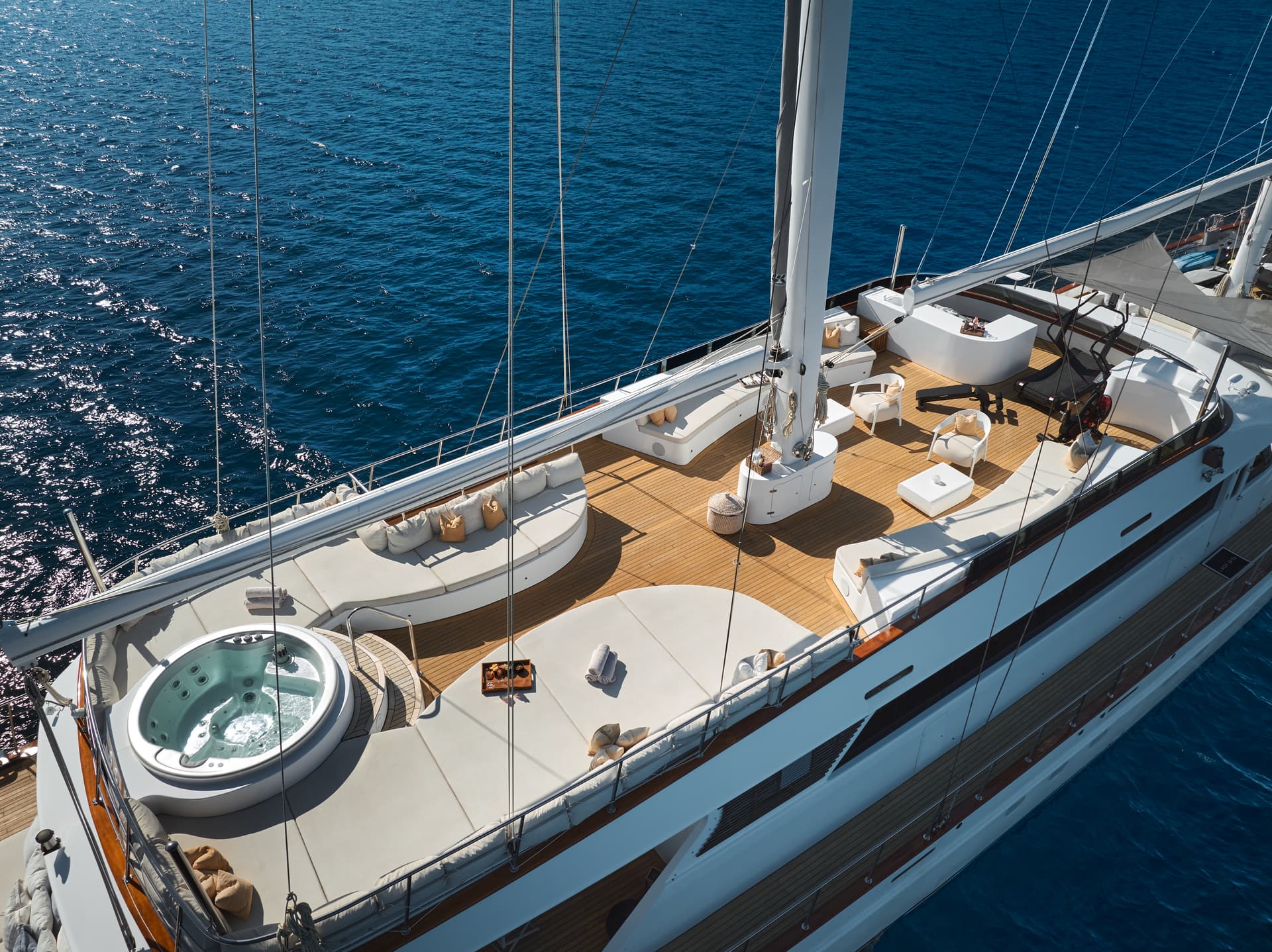 Sundeck of the Lady Gita yacht with teak flooring, jacuzzi, and sun pads on deep blue sea.
