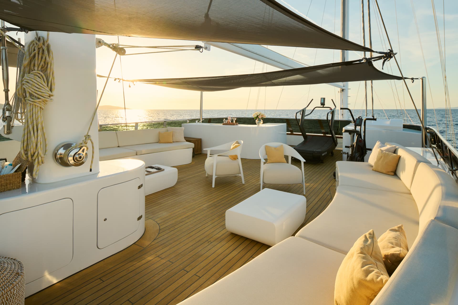 Yacht sundeck with white seating, teak flooring, and ocean view at sunset