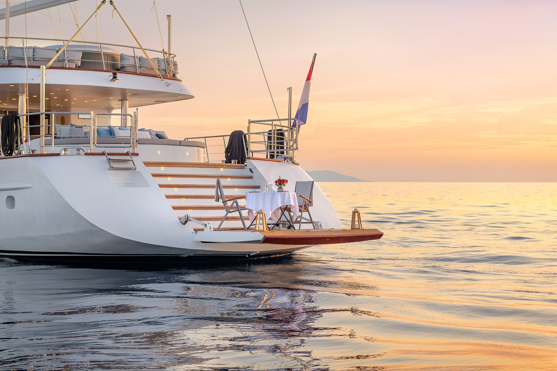 Yacht stern set for romantic dinner on calm sea at sunset with distant island.