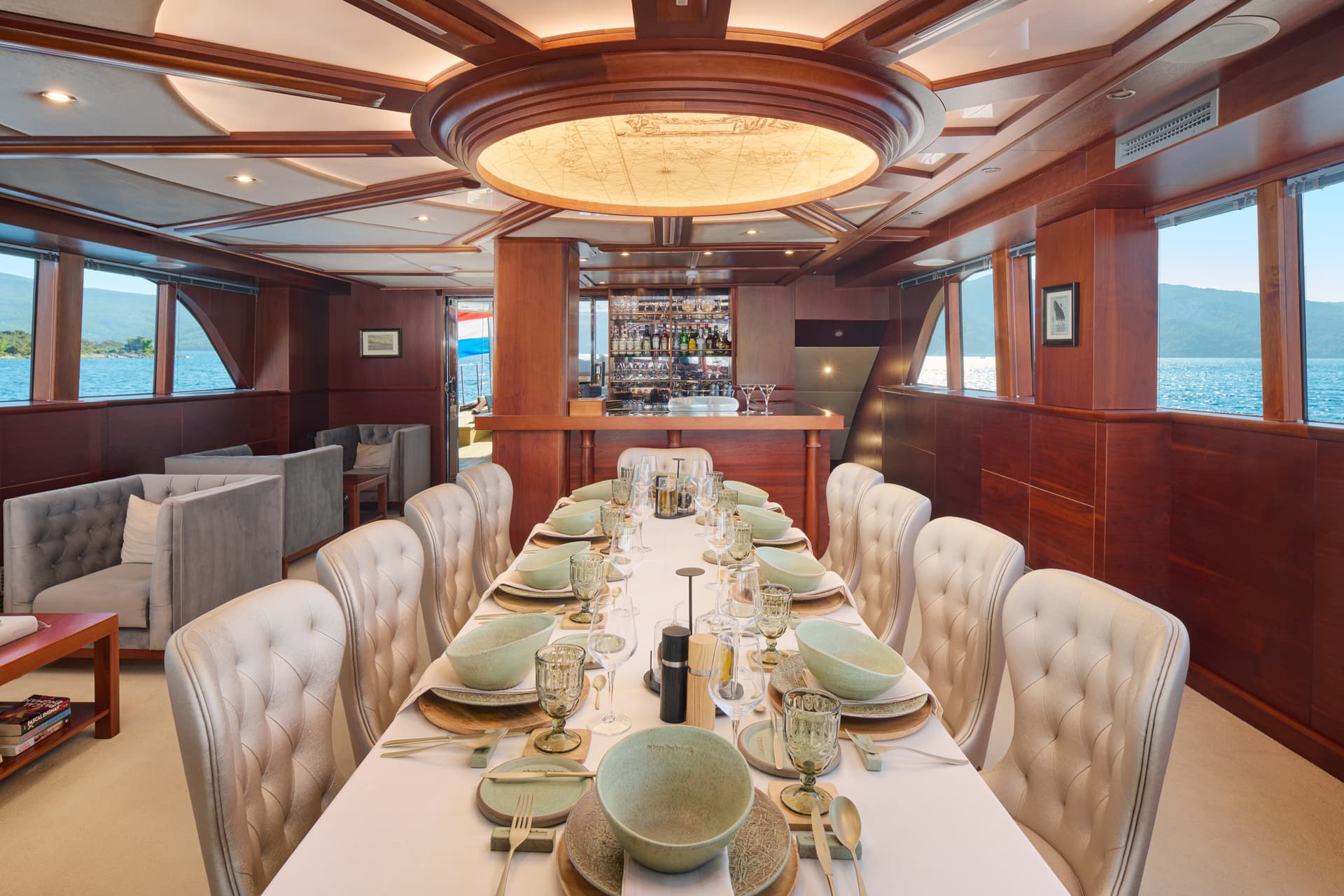 Dining area with formal table setting inside a yacht salon with sea views and a bar.