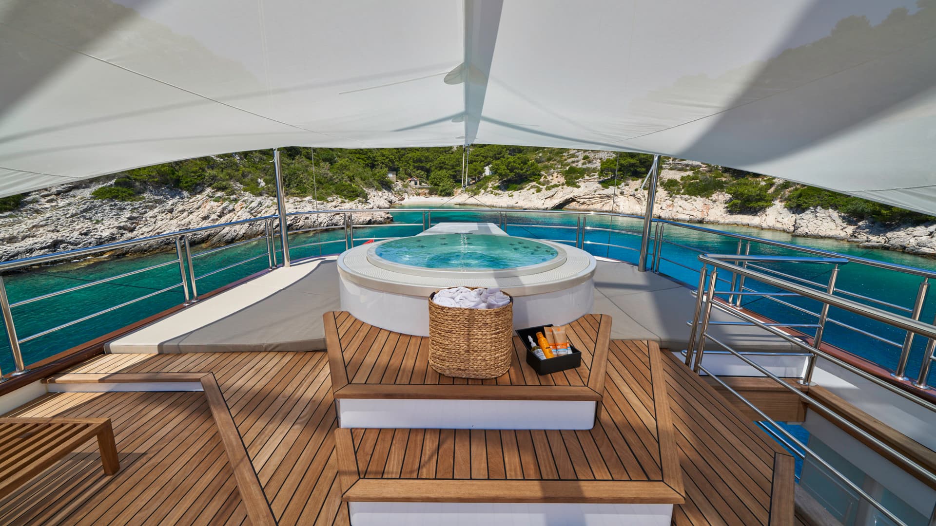 Jacuzzi on yacht deck overlooking turquoise cove with rocky, green coastline