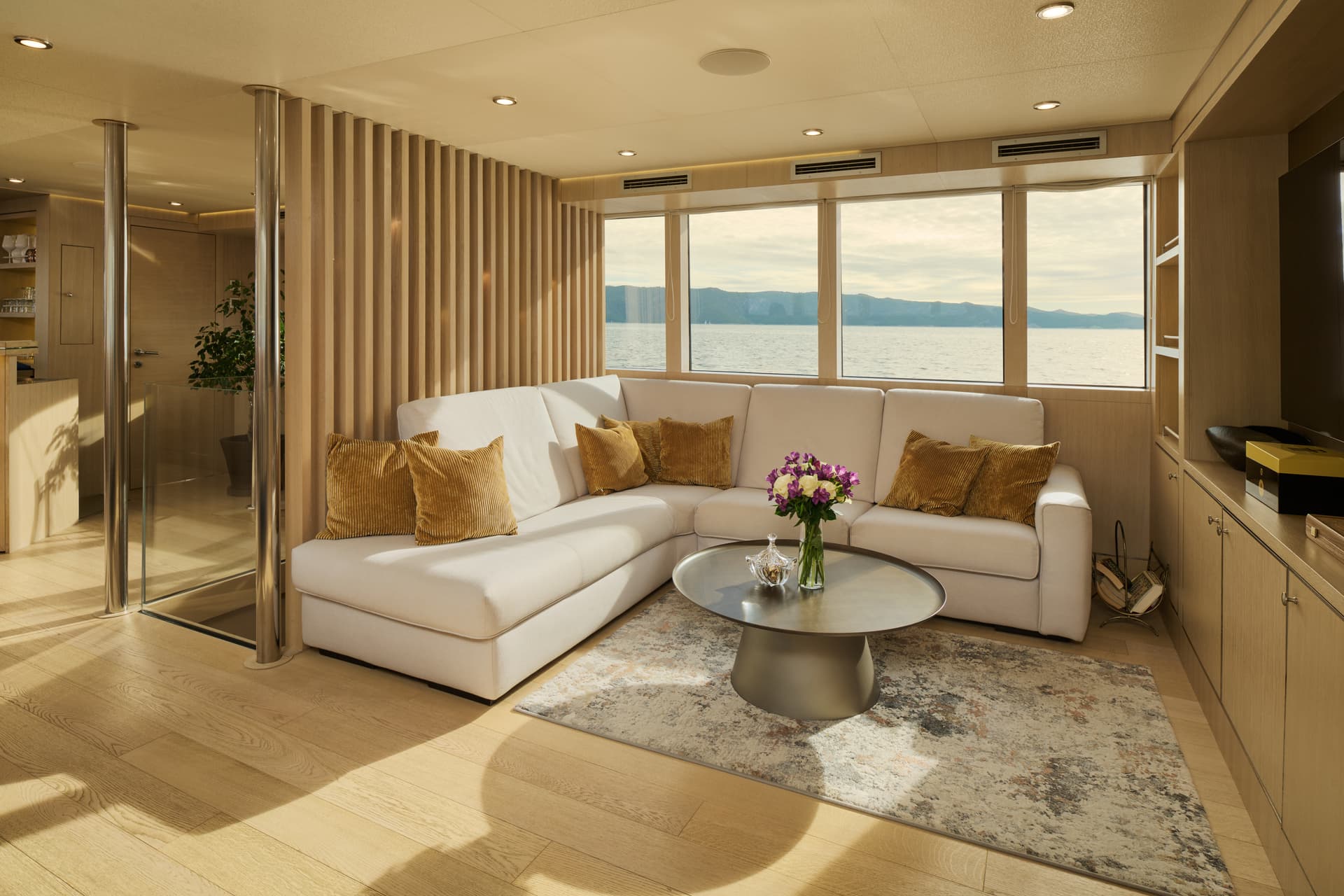 Luxury yacht interior sitting area with white sofa, wood paneling, and sea view.