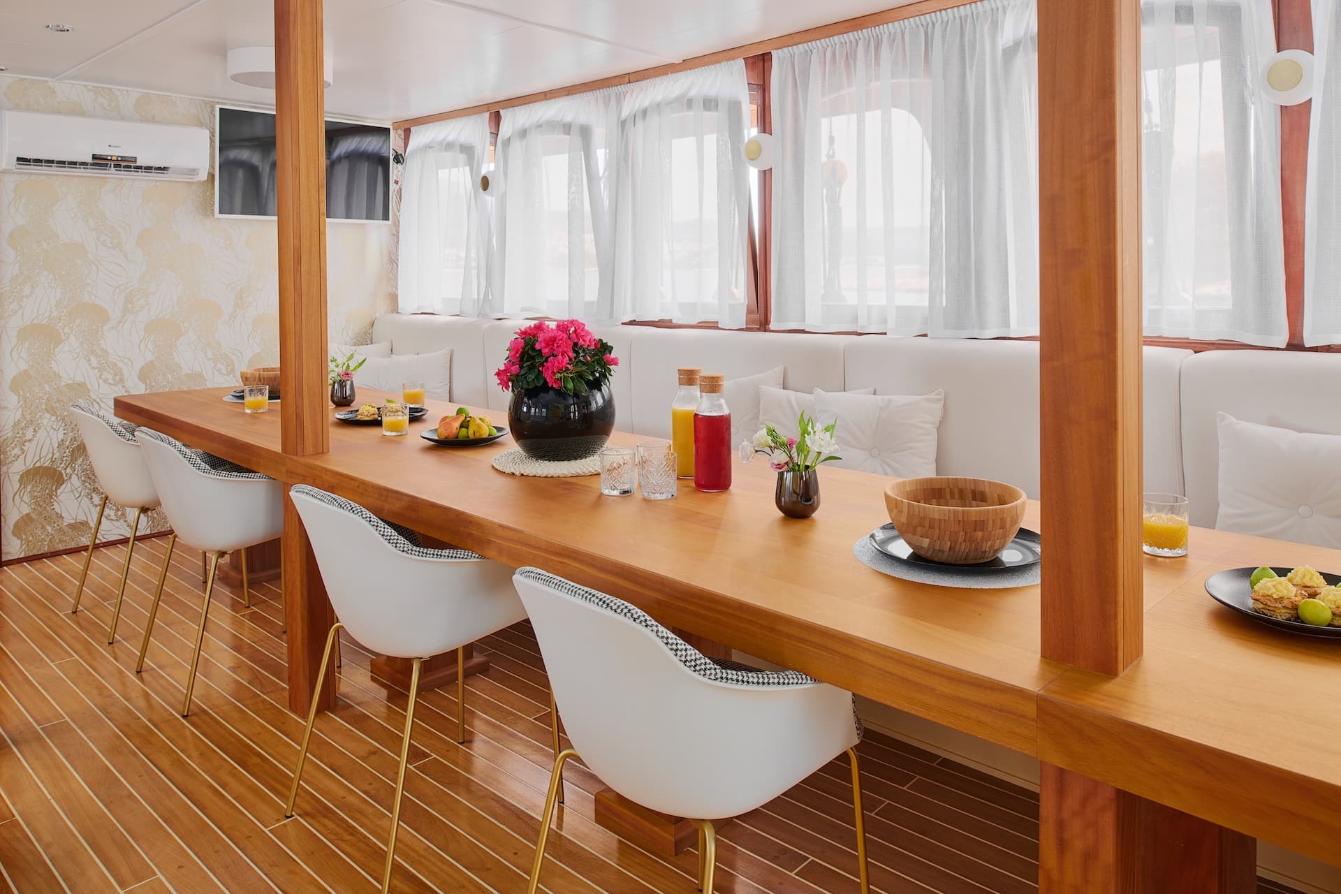 Indoor dining area with wooden table, white chairs, and fruit juice, likely on a yacht.