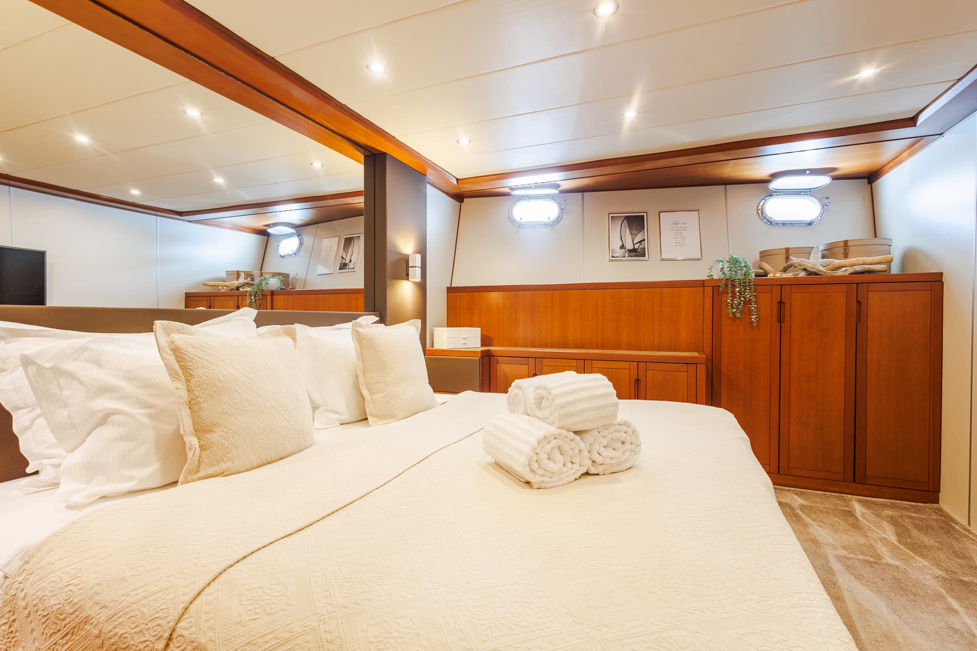 Cabin bedroom with white bedding, wood paneling, and illuminated porthole windows on a boat.