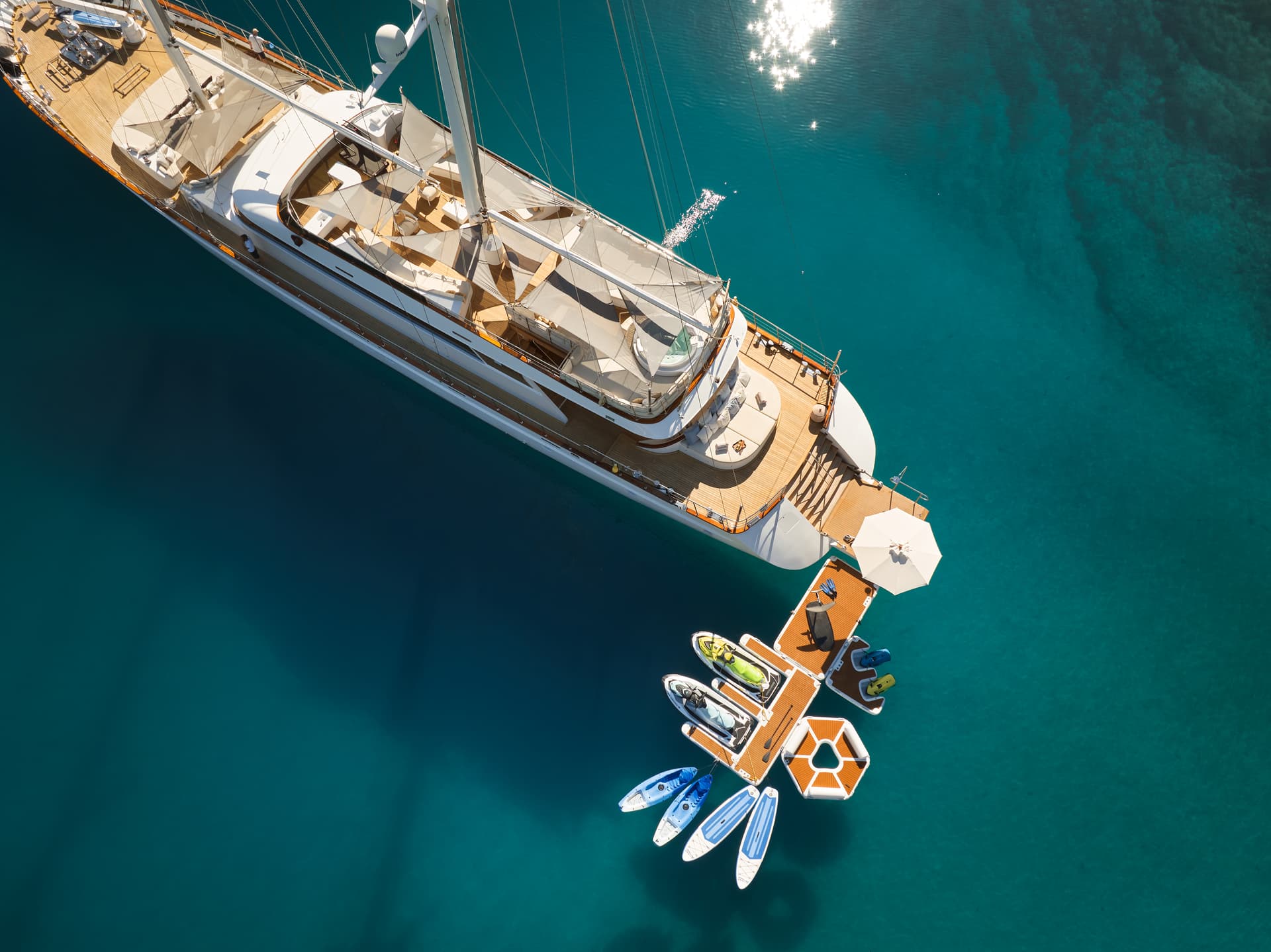 Aerial view of large yacht anchored near water toys and floating dock in turquoise sea.