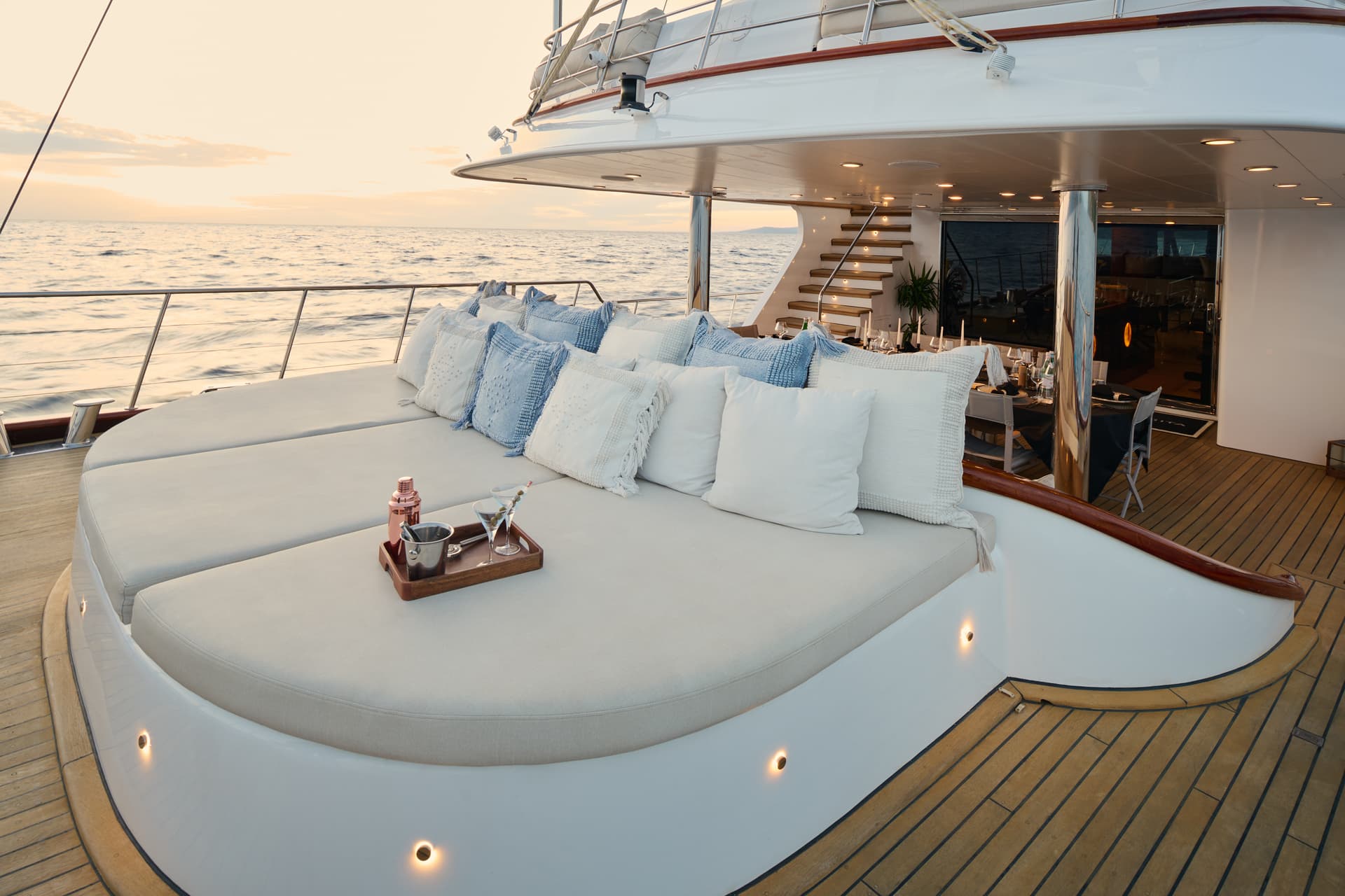 Yacht deck lounge with cocktails, blue and white pillows, overlooking the sea at sunset