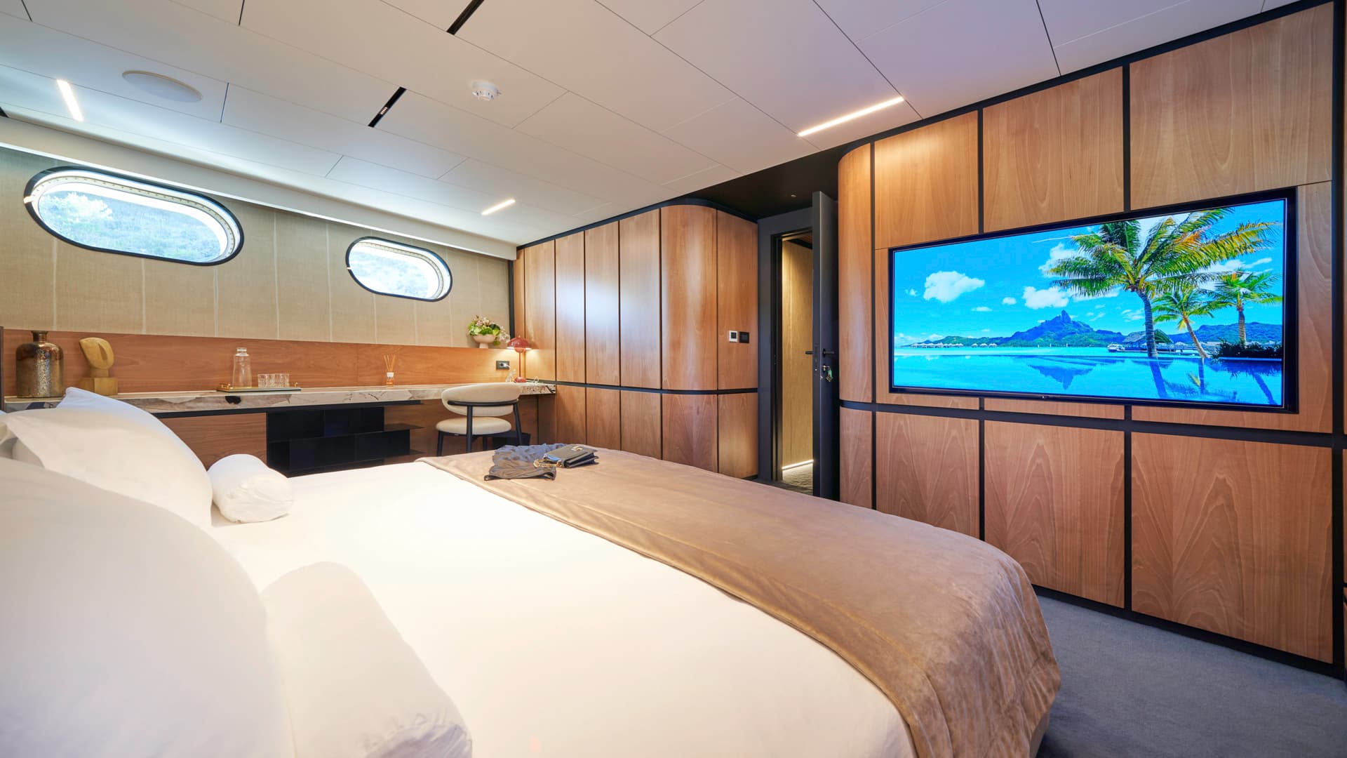 Master cabin interior with white bedding, wood paneling, and oval porthole windows.