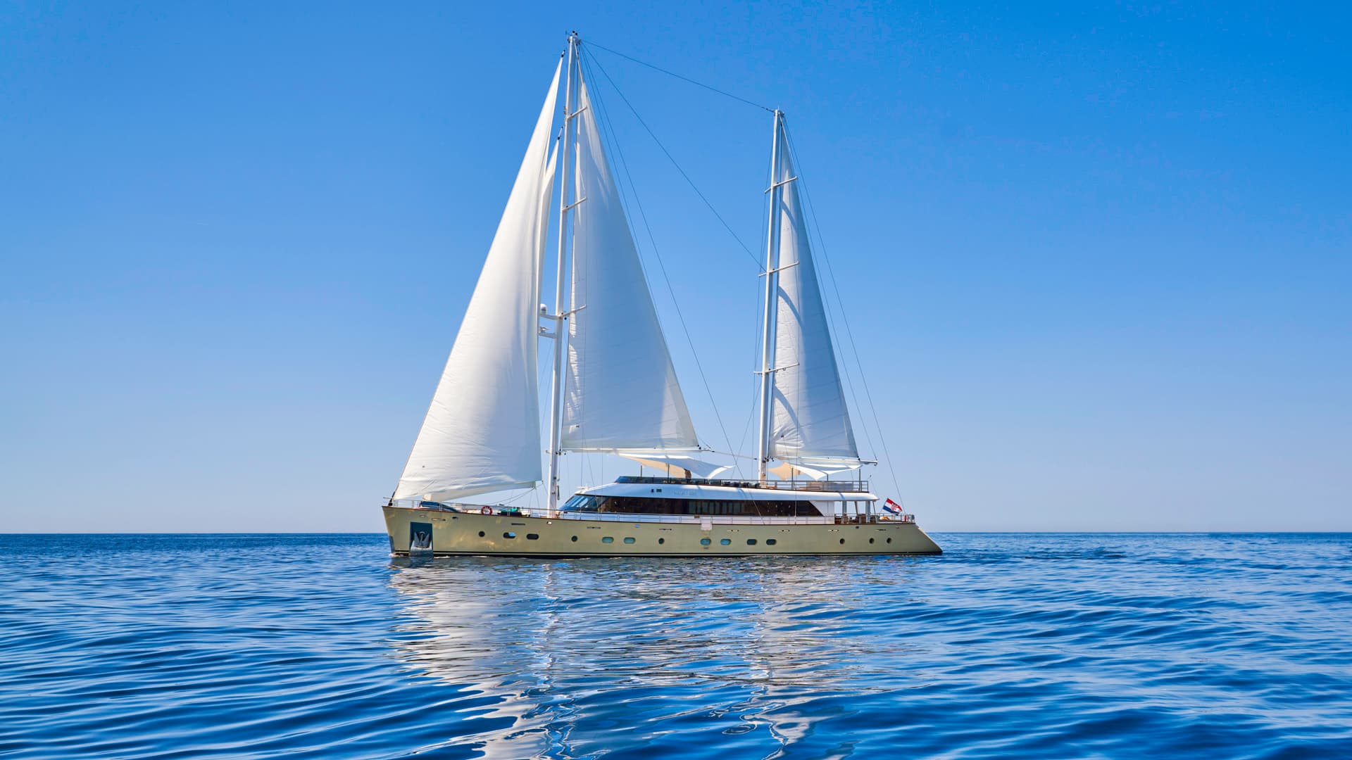 Large sailing yacht with white sails on deep blue, rippling water under clear sky
