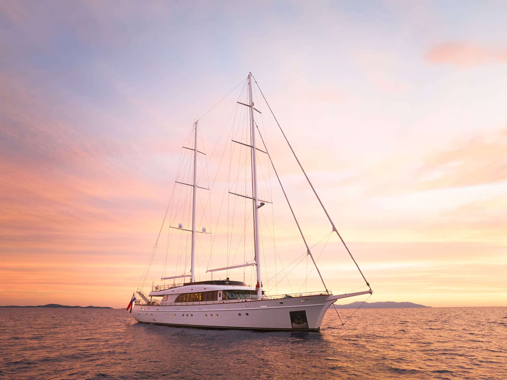Large sailing yacht named Love Story on the water at sunset near distant islands.