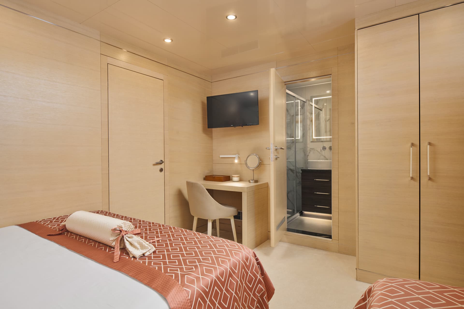 Yacht cabin bedroom with light wood paneling, desk area, and open ensuite bathroom.