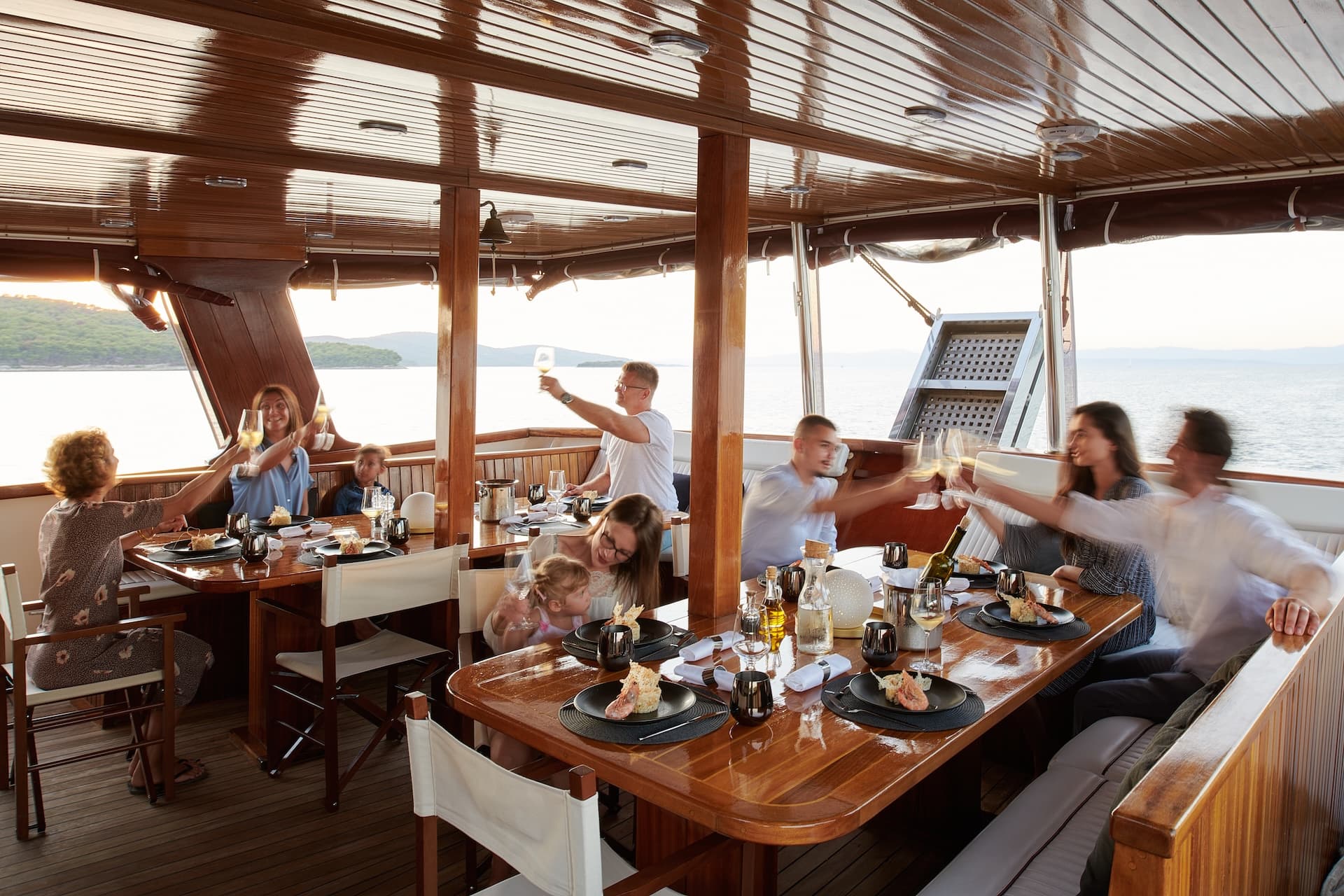 Group toasting with wine glasses on a wooden yacht deck near islands at sunset