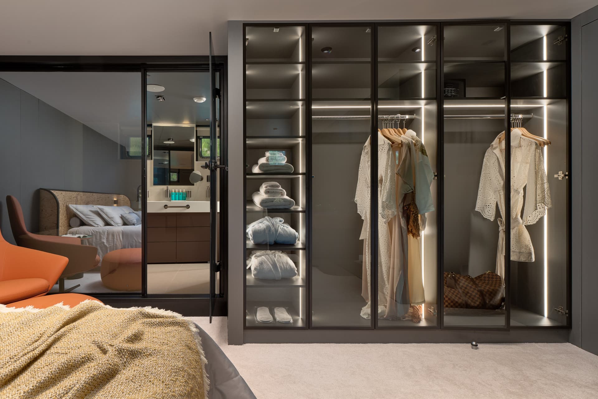 Master cabin interior with illuminated closet, orange chair, and view into bedroom area.