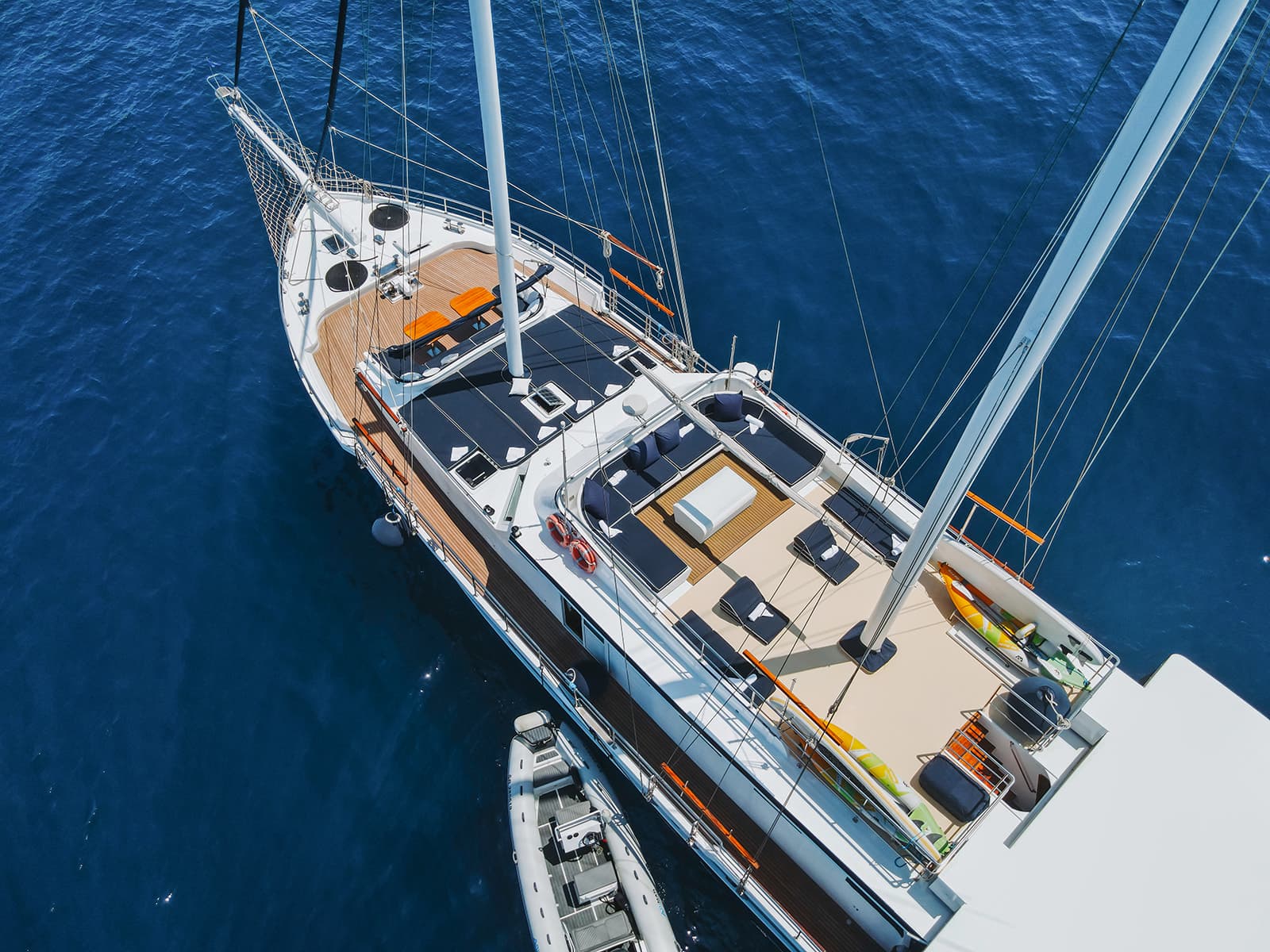 Large sailboat anchored on deep blue water with a small inflatable tender alongside