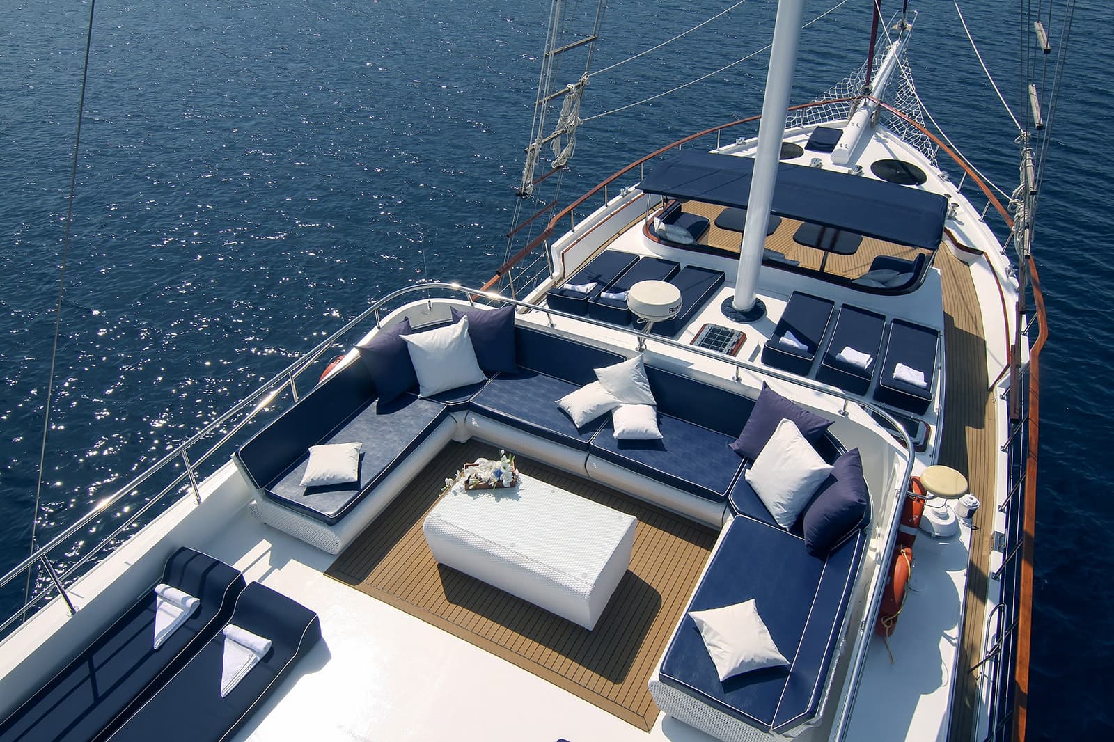 Yacht bow deck with blue and white cushions and teak flooring on sparkling blue sea