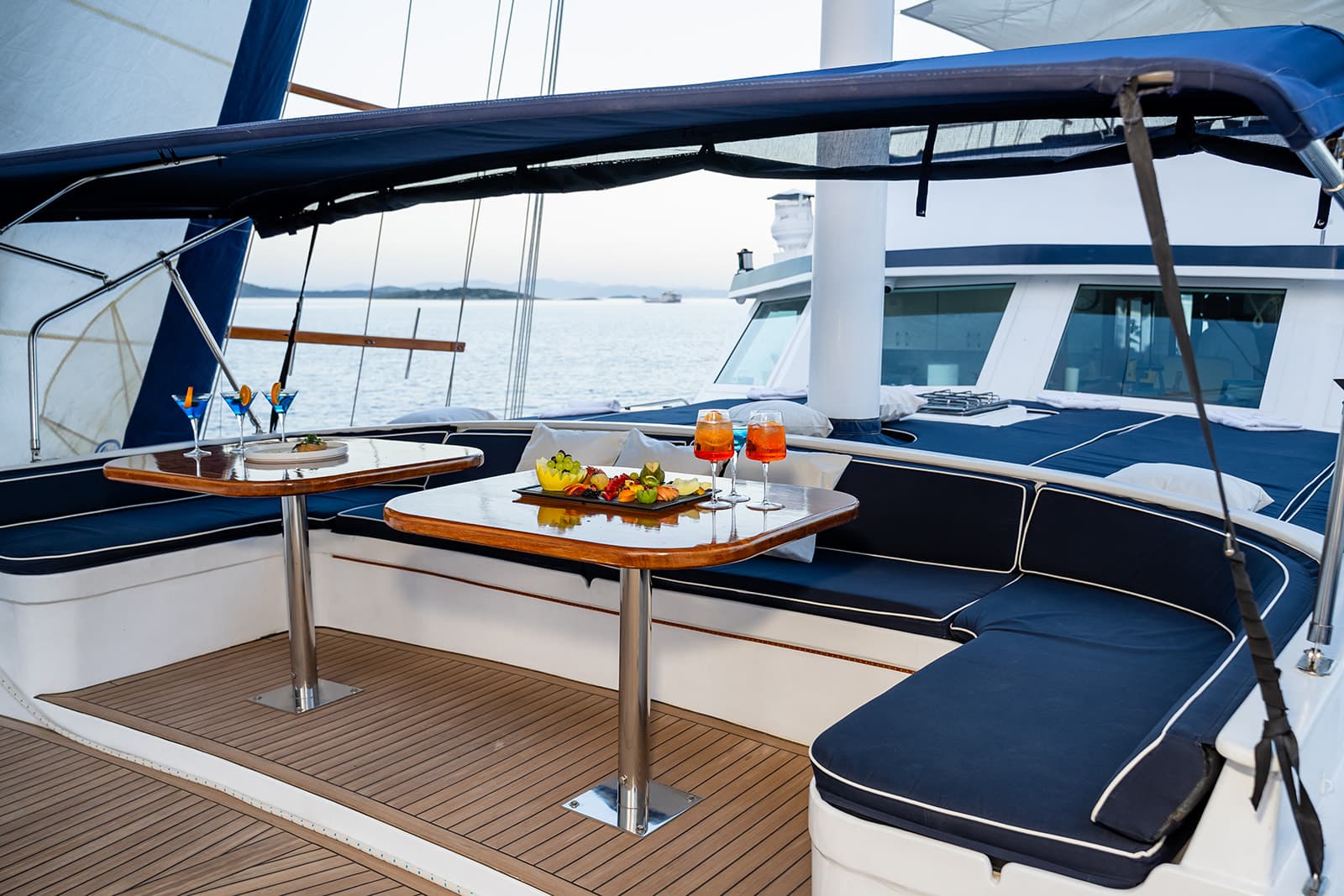Cocktails and fruit platter on teak deck of yacht with sea view and distant islands.