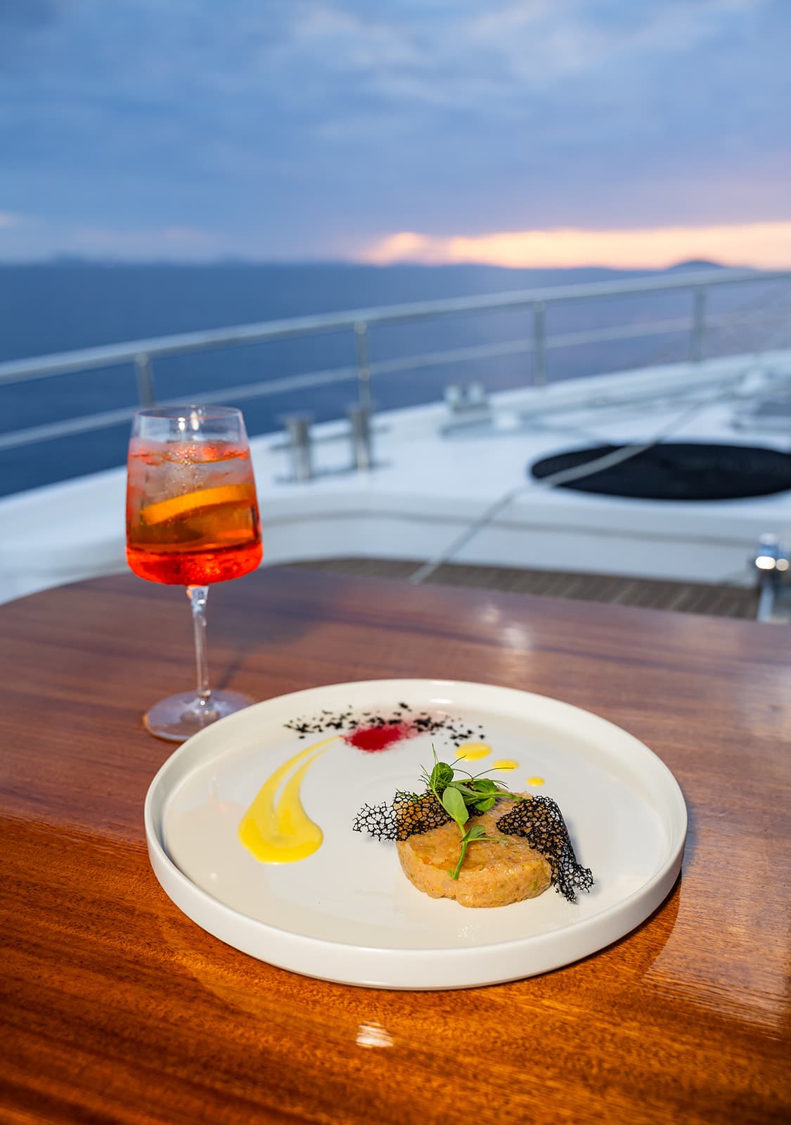 Gourmet appetizer and orange cocktail on yacht deck at sunset over the sea.