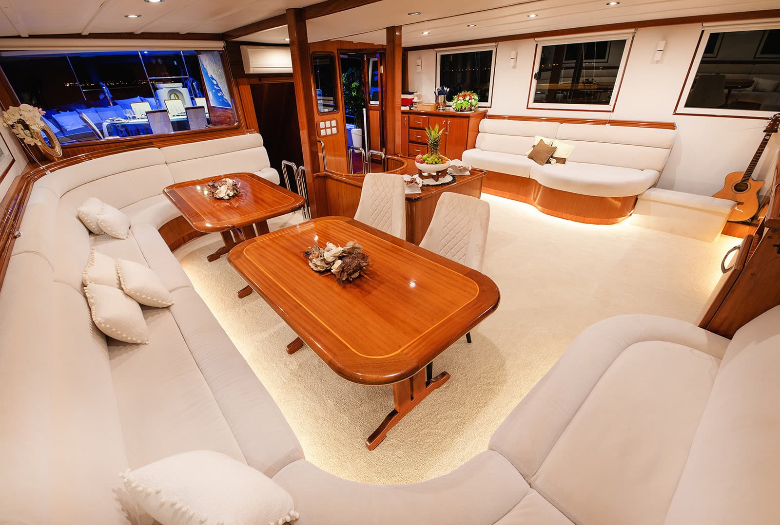 Luxurious yacht interior lounge with cream seating, wood tables, and ambient lighting at night.