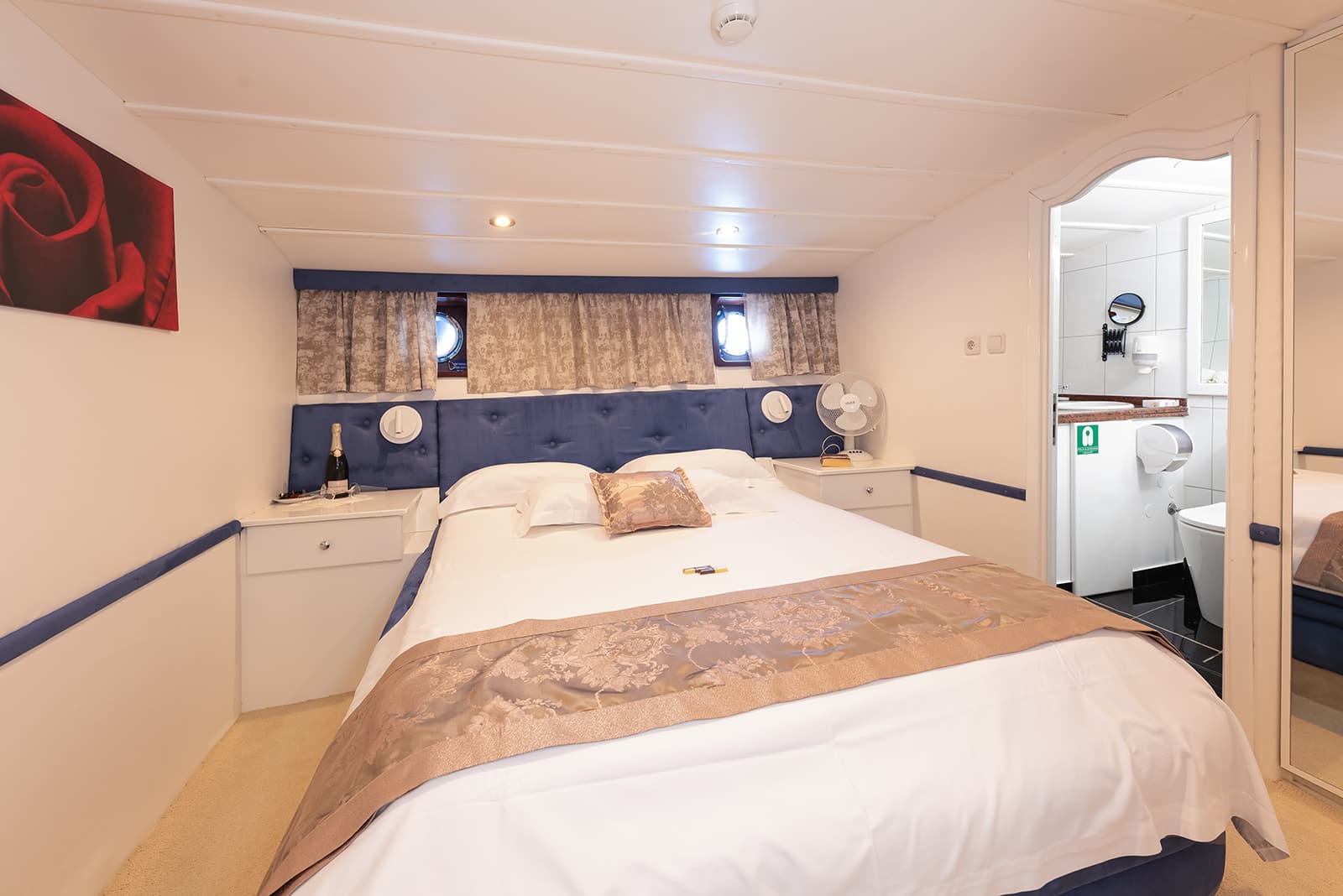 Cabin bedroom with double bed, porthole windows, and view into white bathroom.