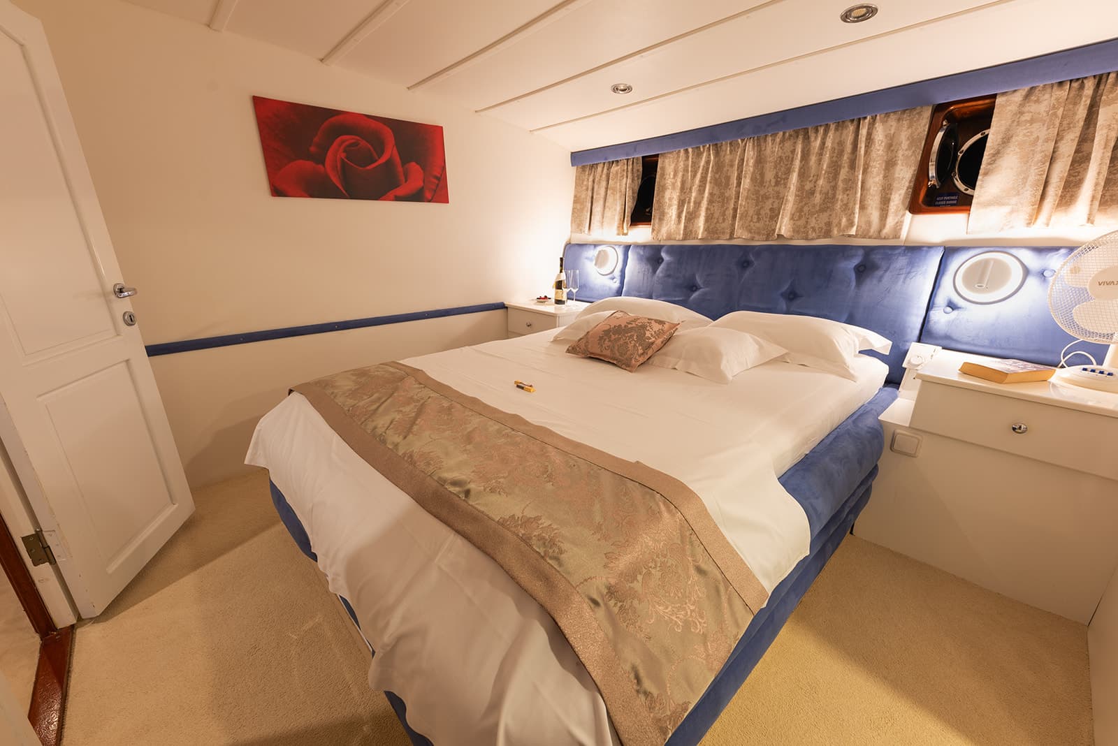 Cozy cabin bedroom with blue upholstered headboard, white bedding, and red rose artwork.