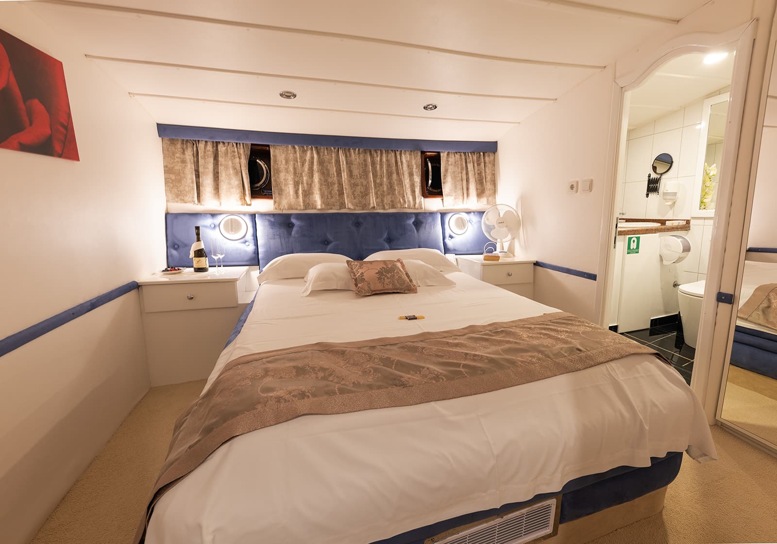 Cabin bedroom with double bed, blue headboard, and ensuite bathroom visible in mirror.