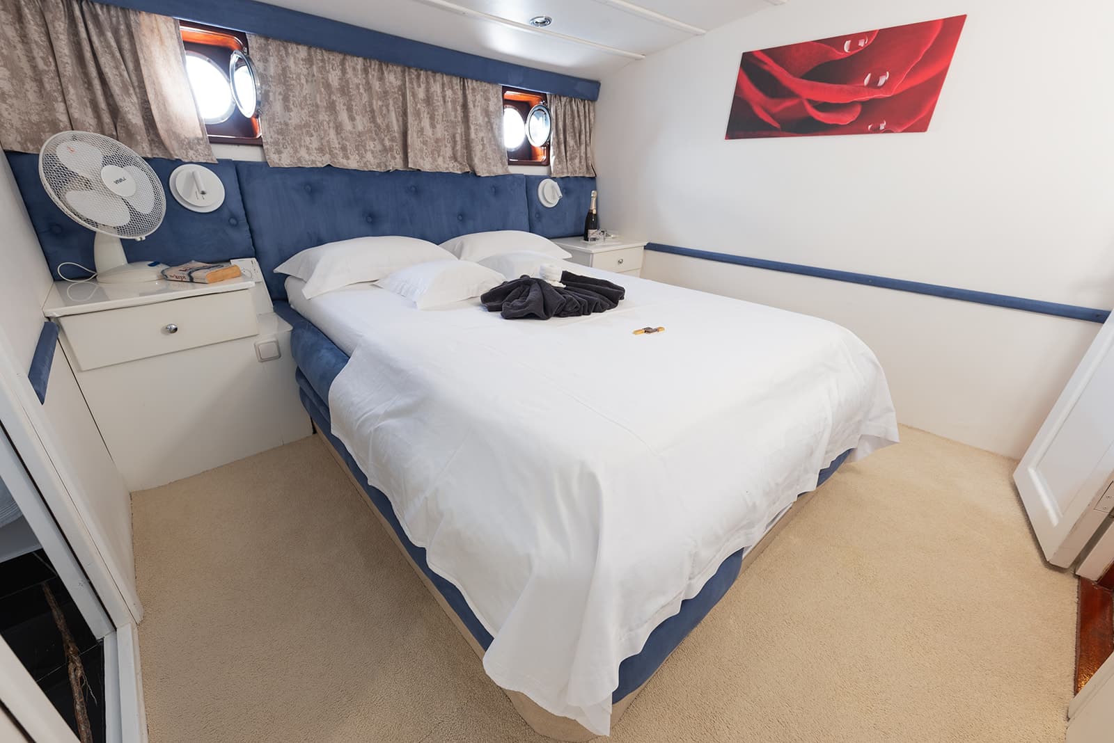 Cabin bedroom with double bed, white linens, blue headboard, and porthole windows.
