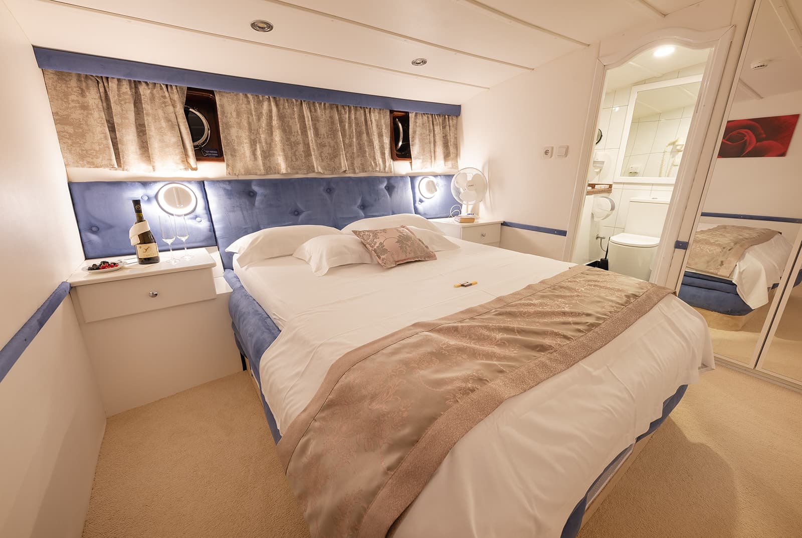 Cabin bedroom with double bed, blue headboard, and ensuite bathroom visible in mirror reflection.