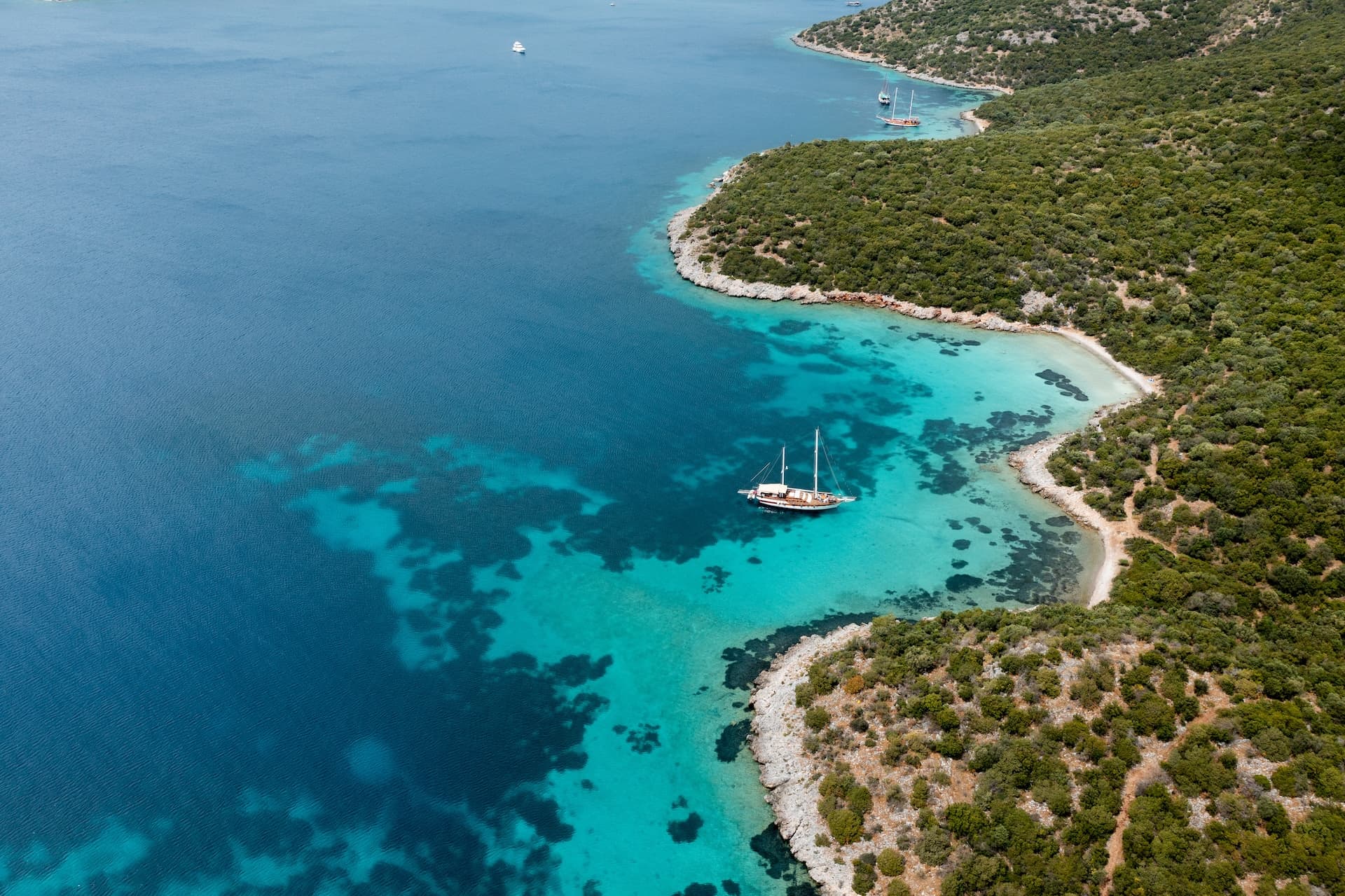 Sailboats anchored in clear turquoise water near a rocky, green coastline of the Croatian coast.