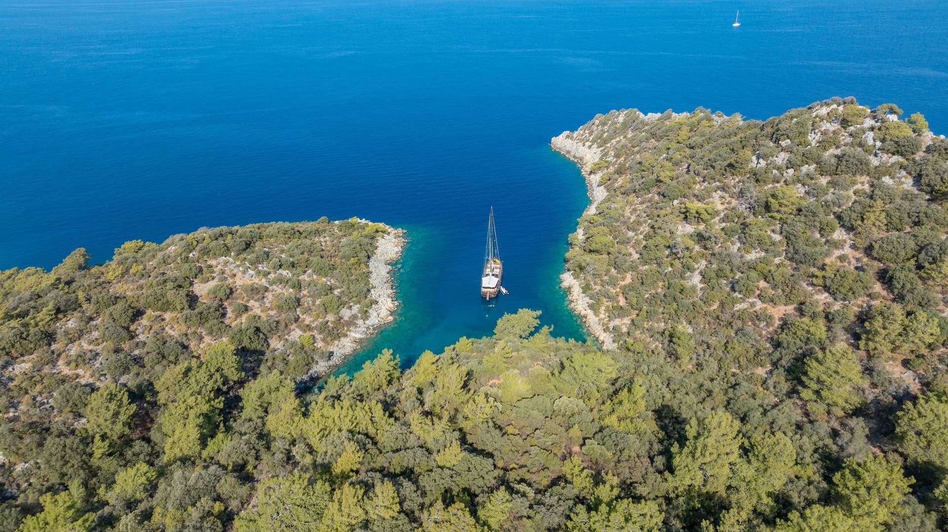 Sailboat anchored in a narrow cove with turquoise water and forested coastline.