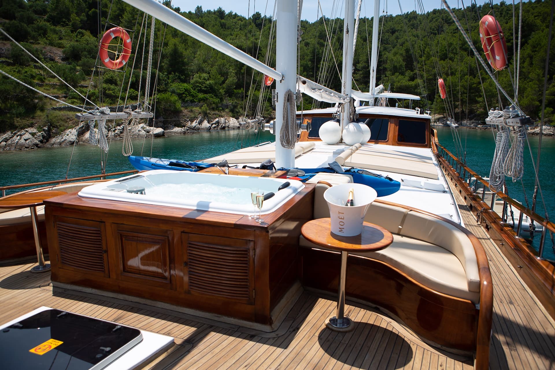 Jacuzzi and champagne on wooden yacht deck anchored near forested coastline