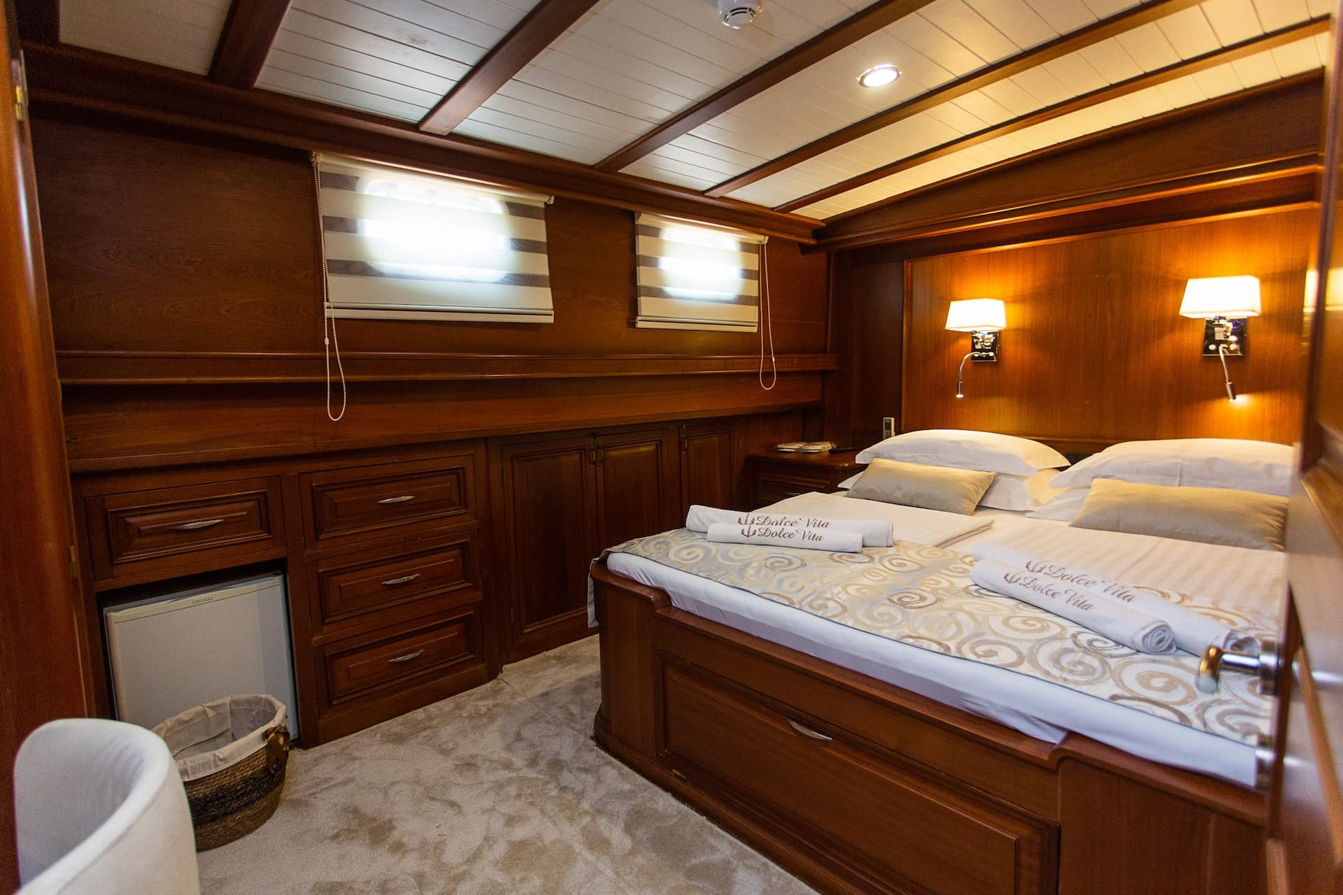 Double cabin bedroom with wood paneling, plush bedding, and bright windows on a yacht.
