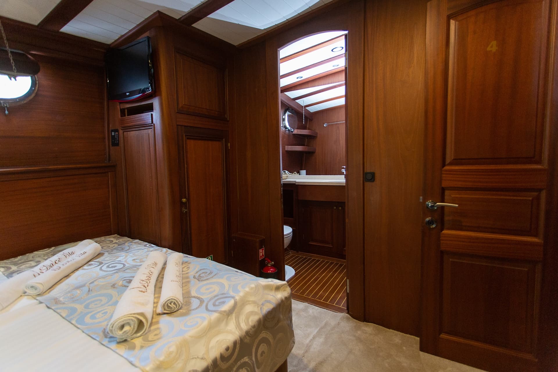 Cabin interior with wood paneling, bed, TV, and doorway leading to a bathroom.