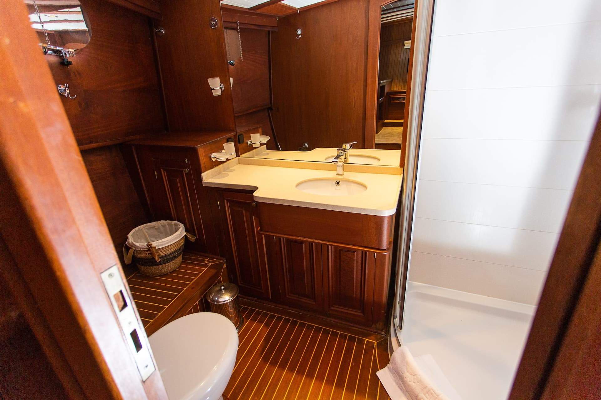 Ensuite bathroom with rich wood paneling, vanity, and white shower stall, likely on a yacht.