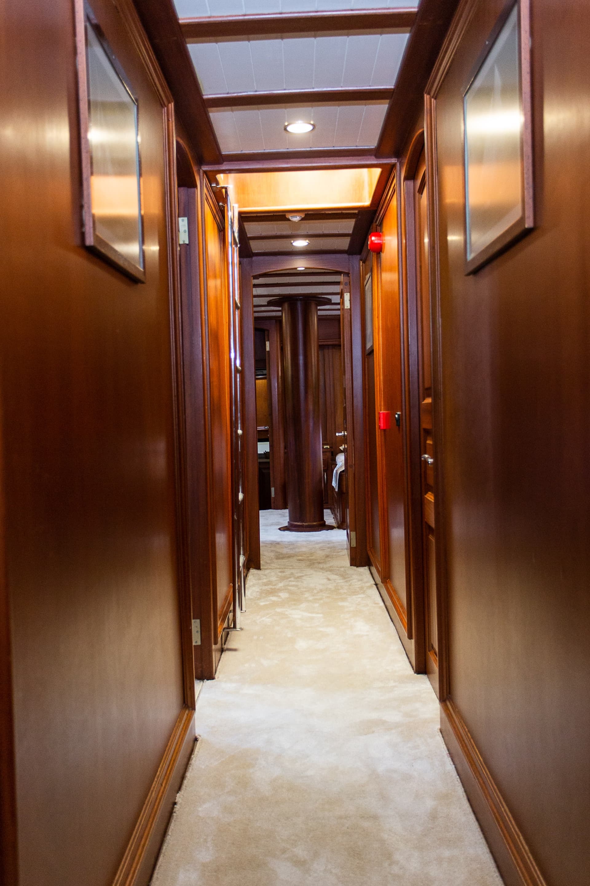 Hallway interior with polished dark wood paneling and light carpet, leading toward a central pillar.