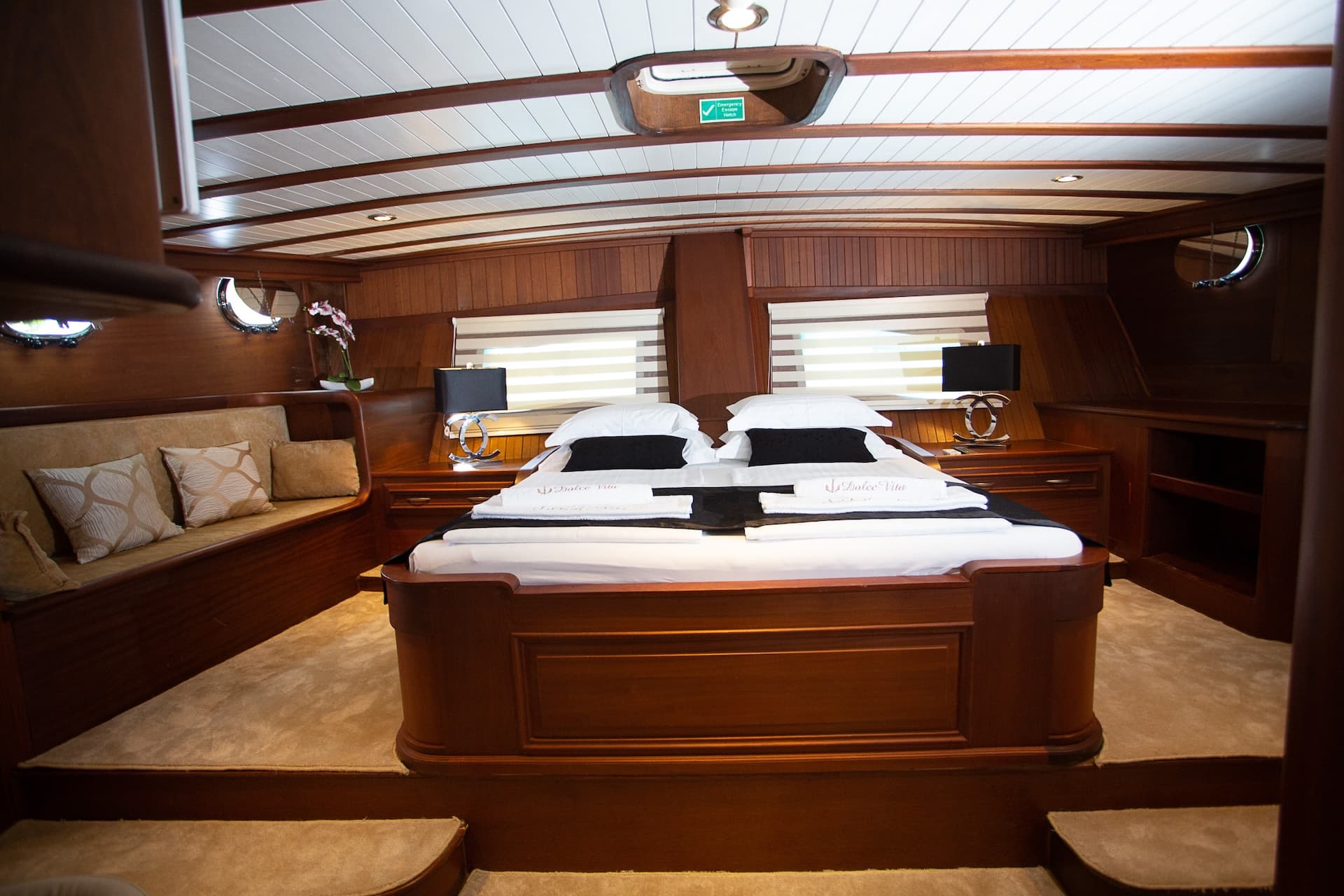 Master bedroom cabin with rich wood paneling, double bed, and built-in seating on a yacht.