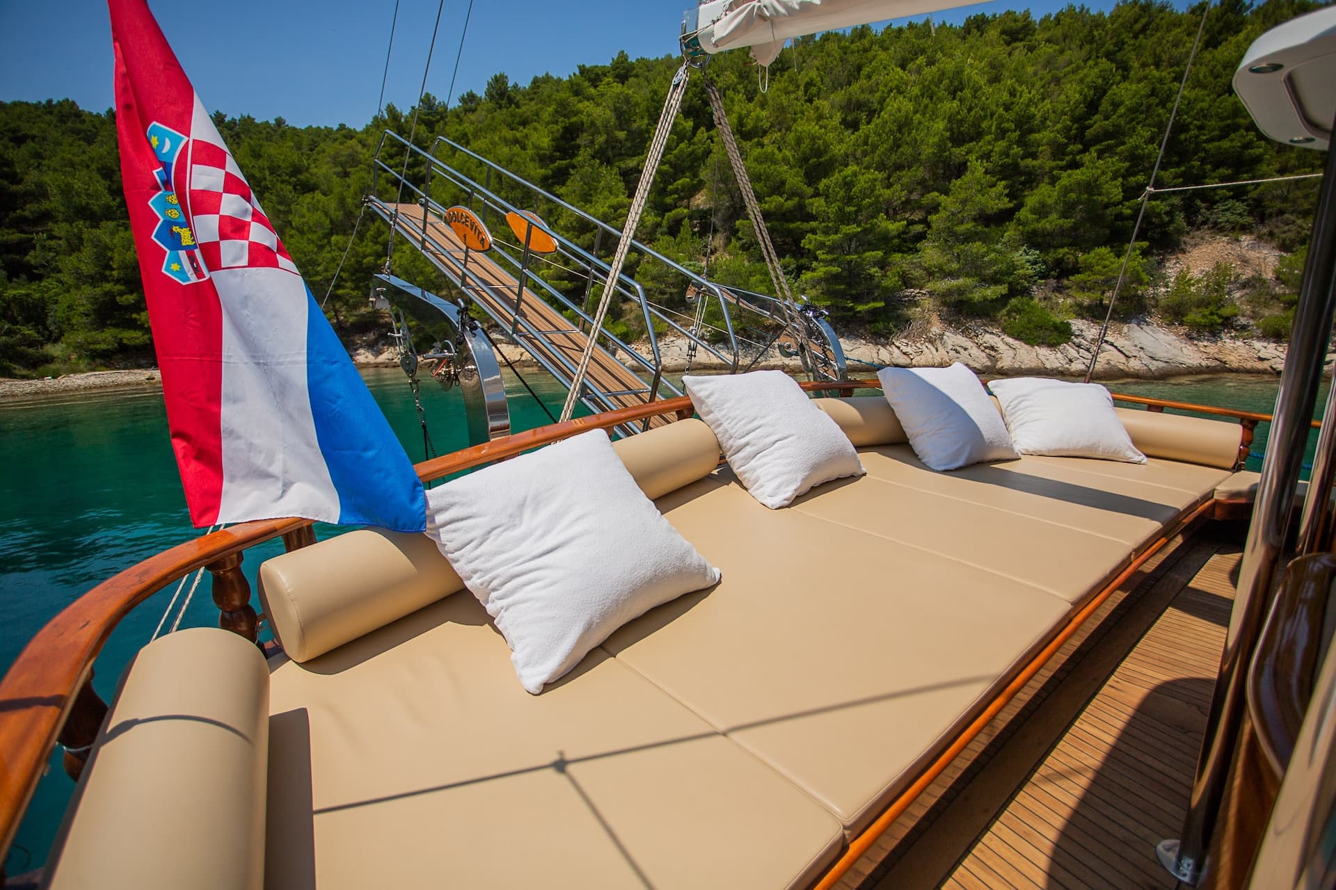 Croatian flag on boat deck with sunbathing cushions near forested coastline