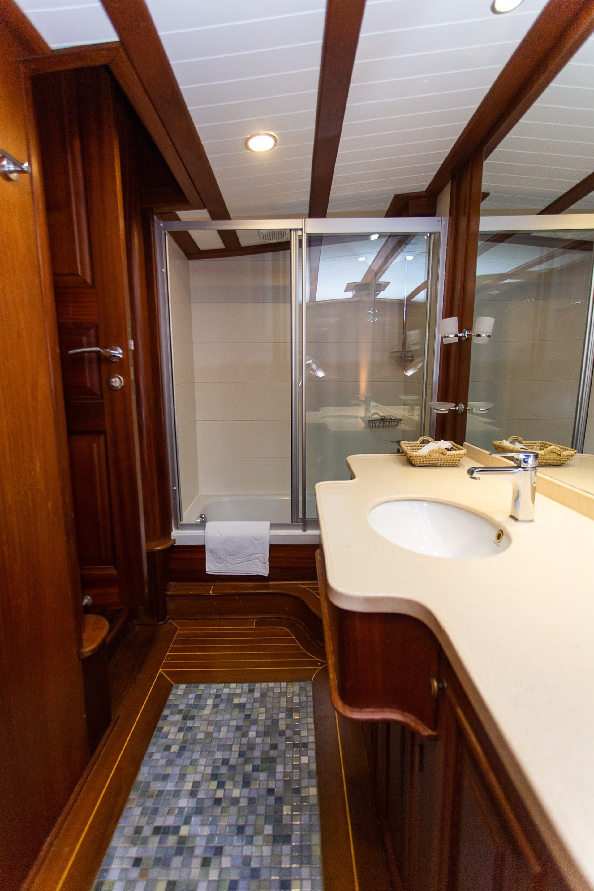 Bathroom with wood paneling, vanity, sink, and glass shower stall, likely on a boat.