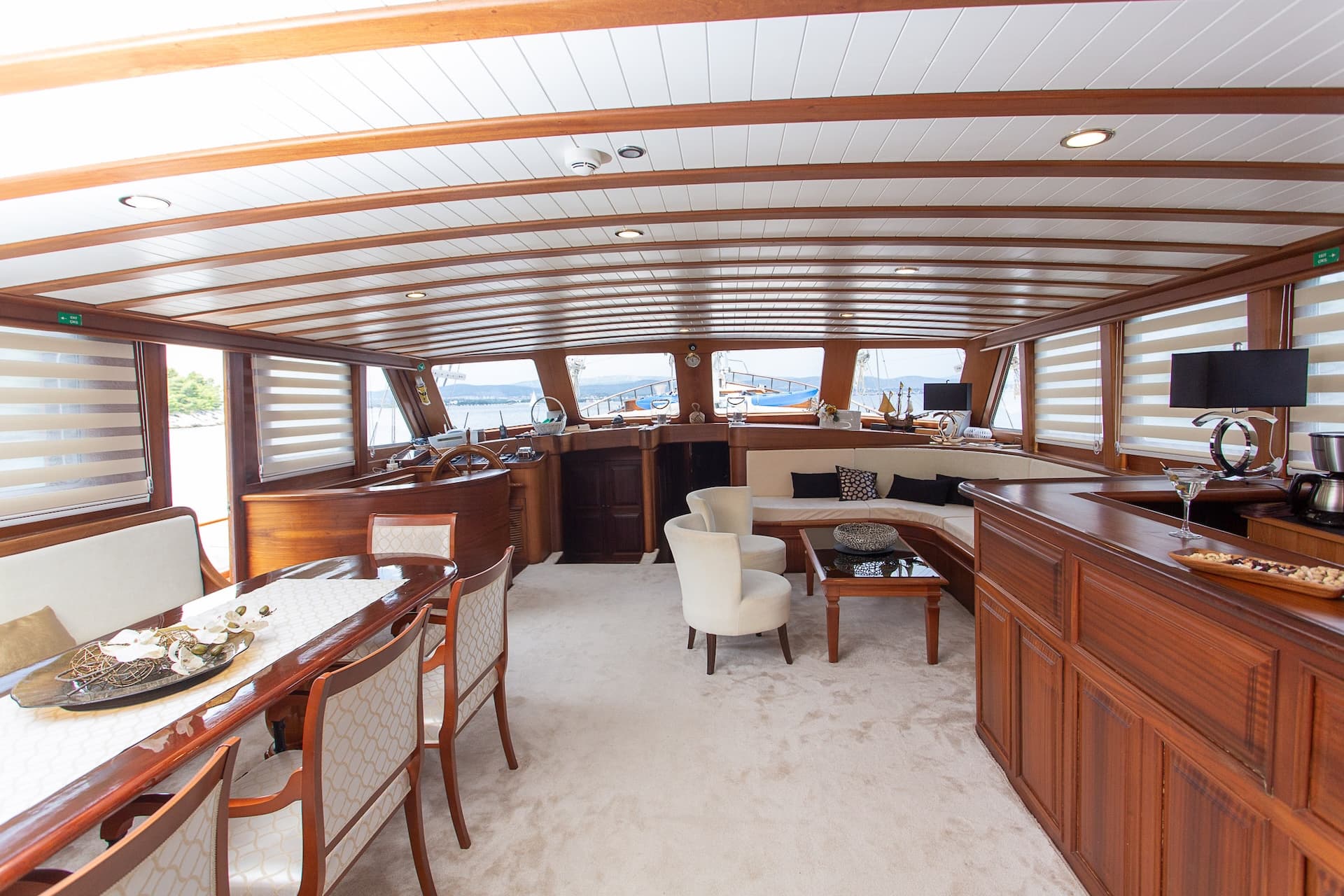 Spacious yacht salon with wood paneling, dining area, lounge, and helm station overlooking the water.