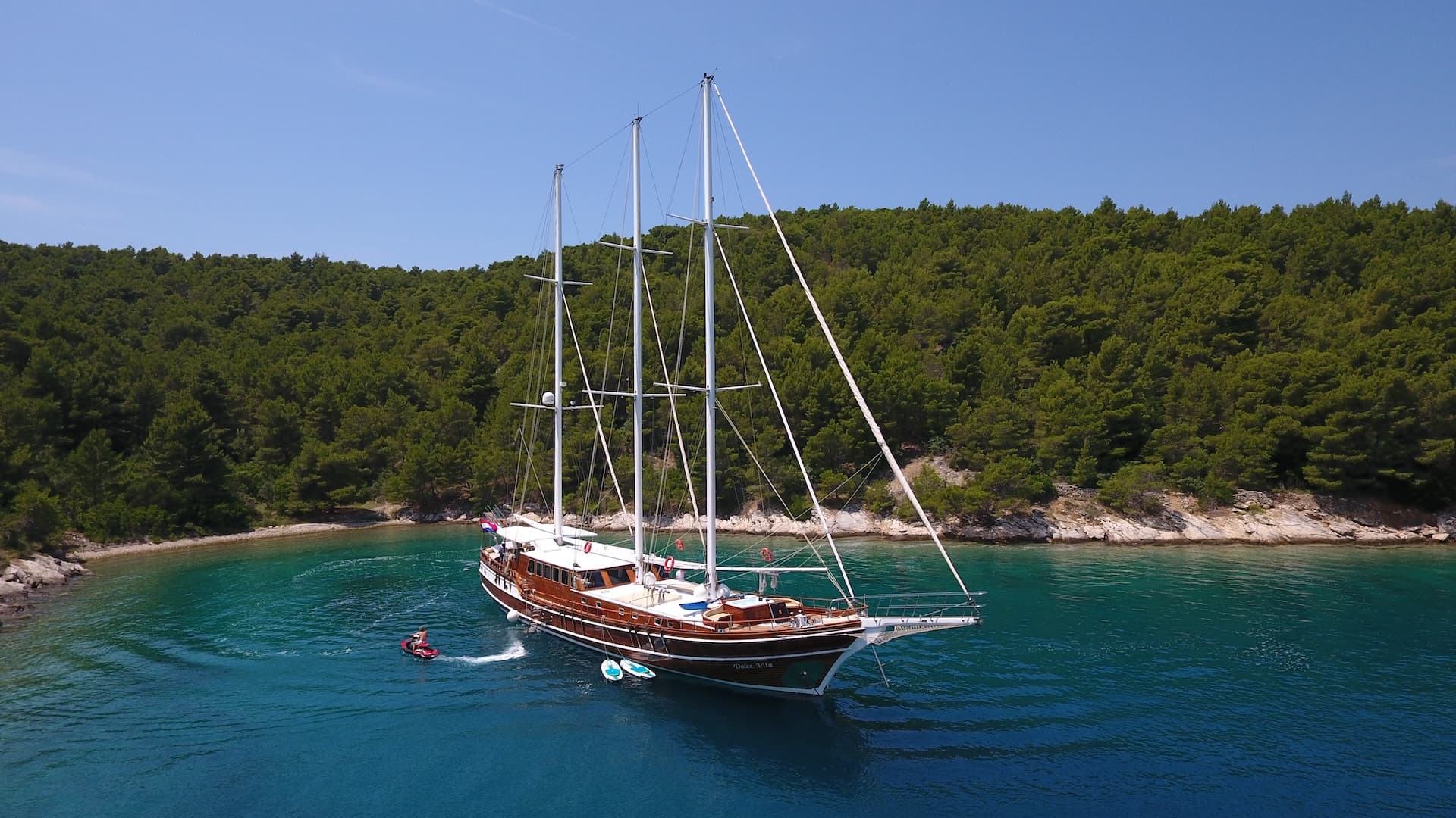 Wooden gulet yacht Dolce Vita anchored in turquoise cove near forested coastline
