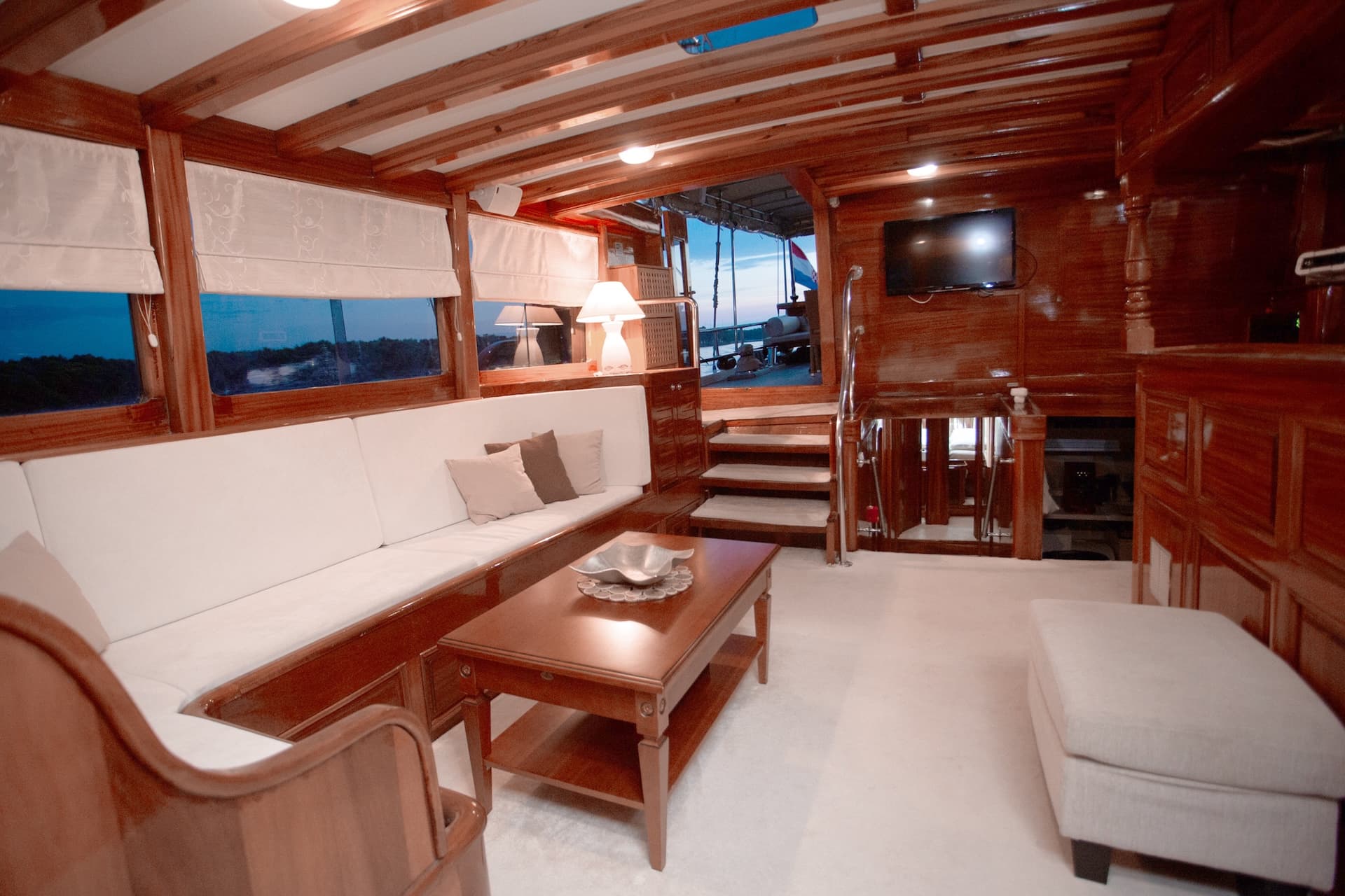 Cozy yacht interior with rich wood paneling, white seating, and view of the deck.