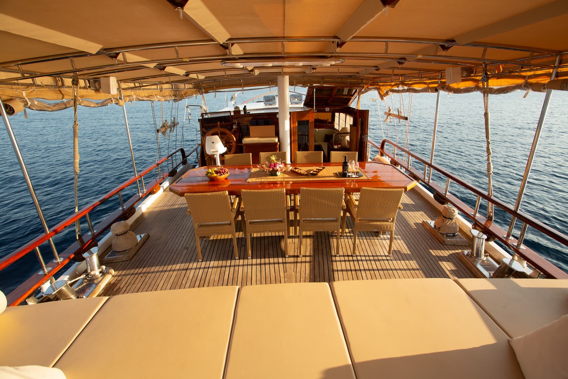 Deck dining area with wicker chairs and wooden table on a boat sailing on blue water.