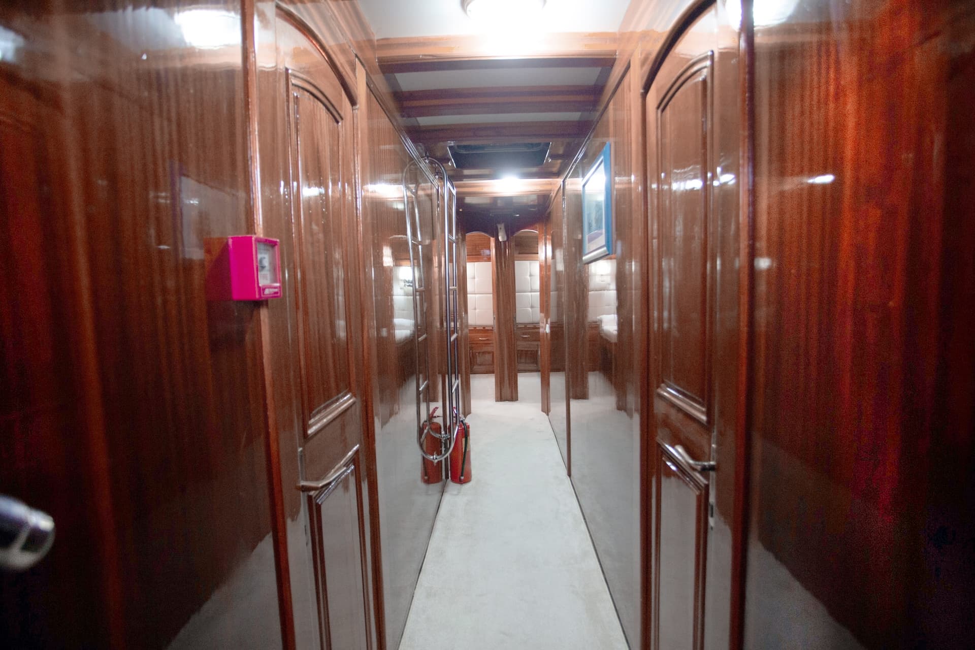 Hallway with glossy dark wood paneling and doors, likely on a boat or ship.