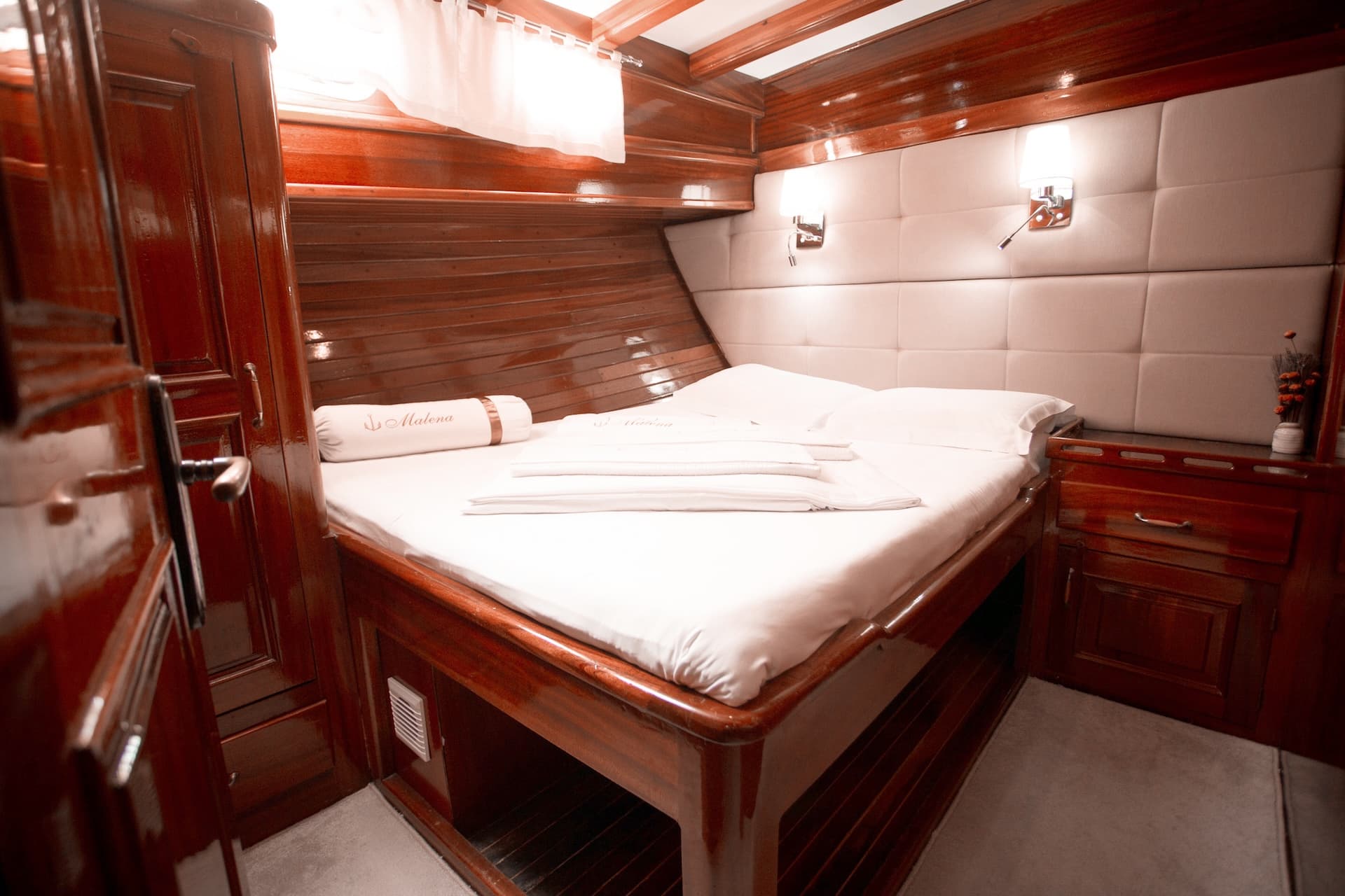 Double bed cabin with glossy wood paneling and white linens on a boat named Malena.