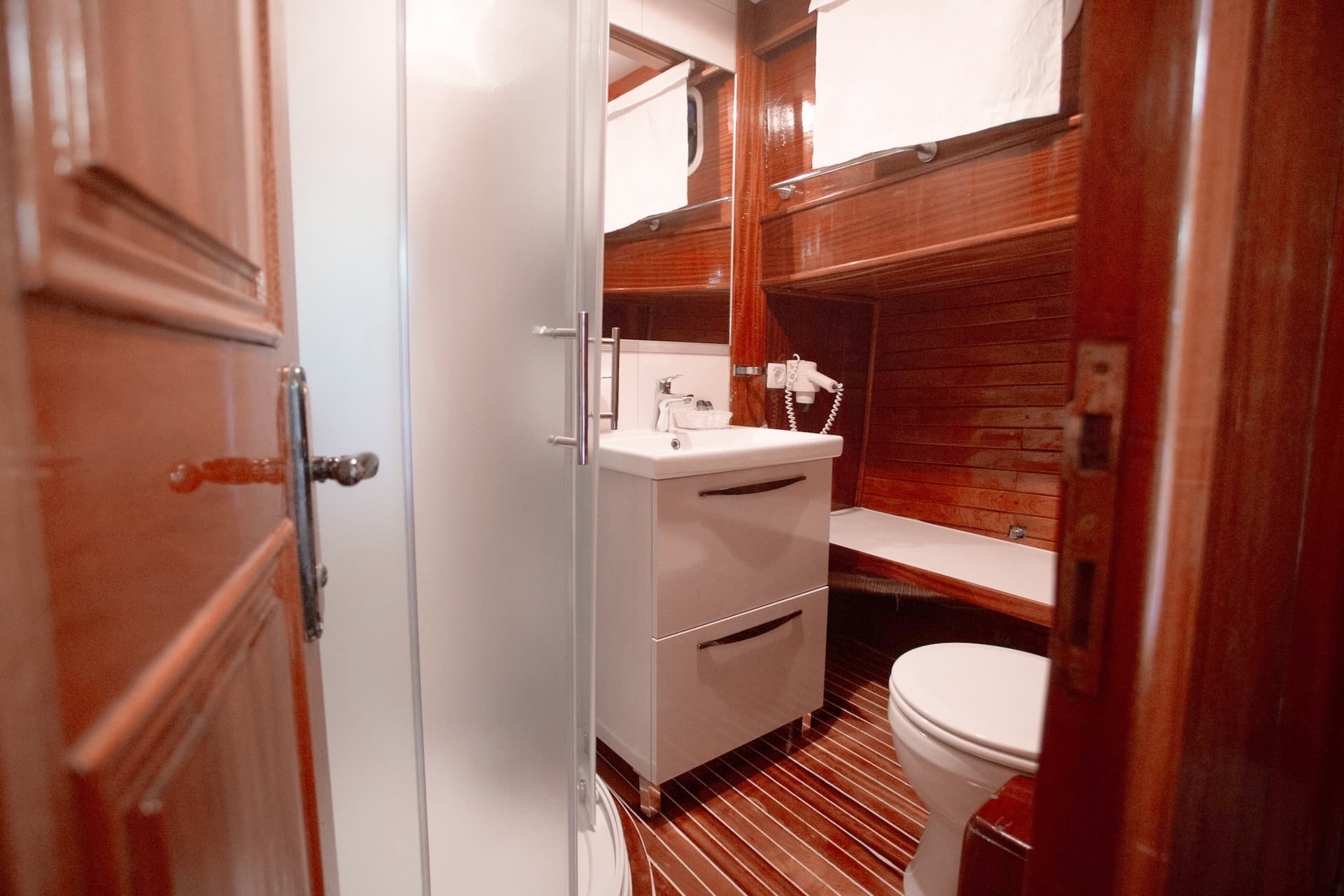 Compact bathroom with white vanity, toilet, and wood paneling inside a boat cabin.