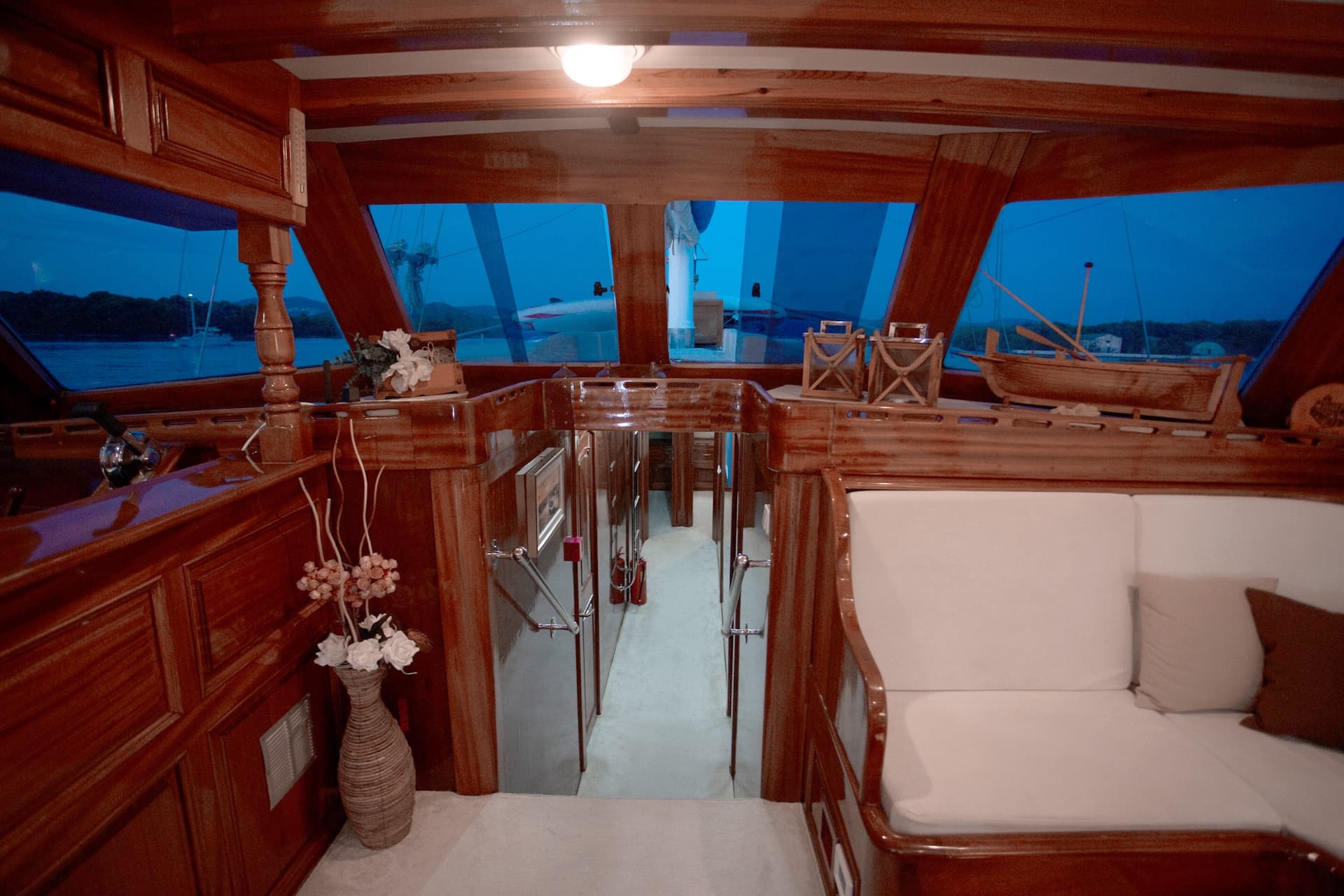 Interior cabin of wooden yacht with white seating and view of dark blue water.