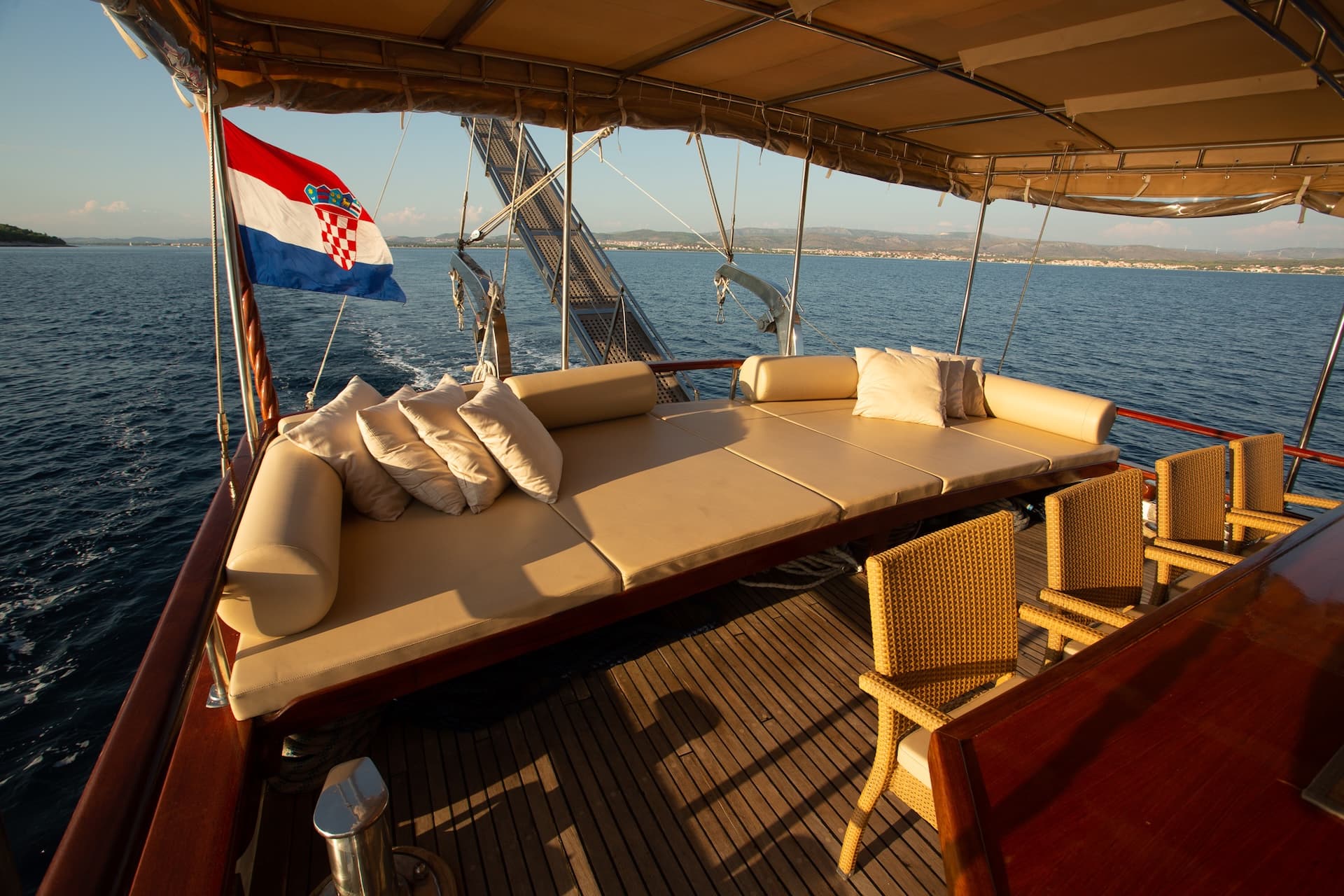 Boat deck with sunbed and Croatian flag sailing on blue sea toward coastline.